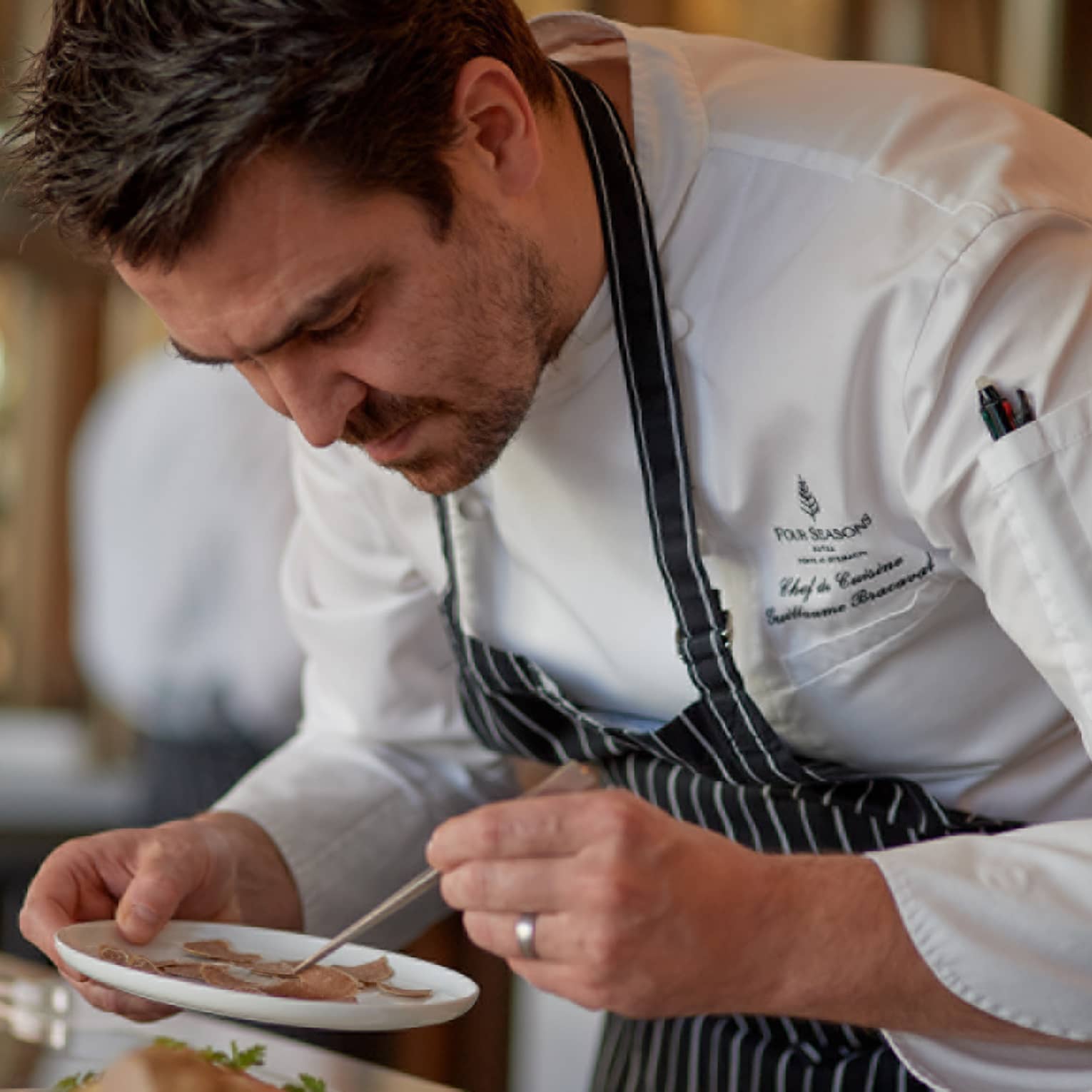 Four Seasons chef in striped apron carefully plating a dish in a kitchen