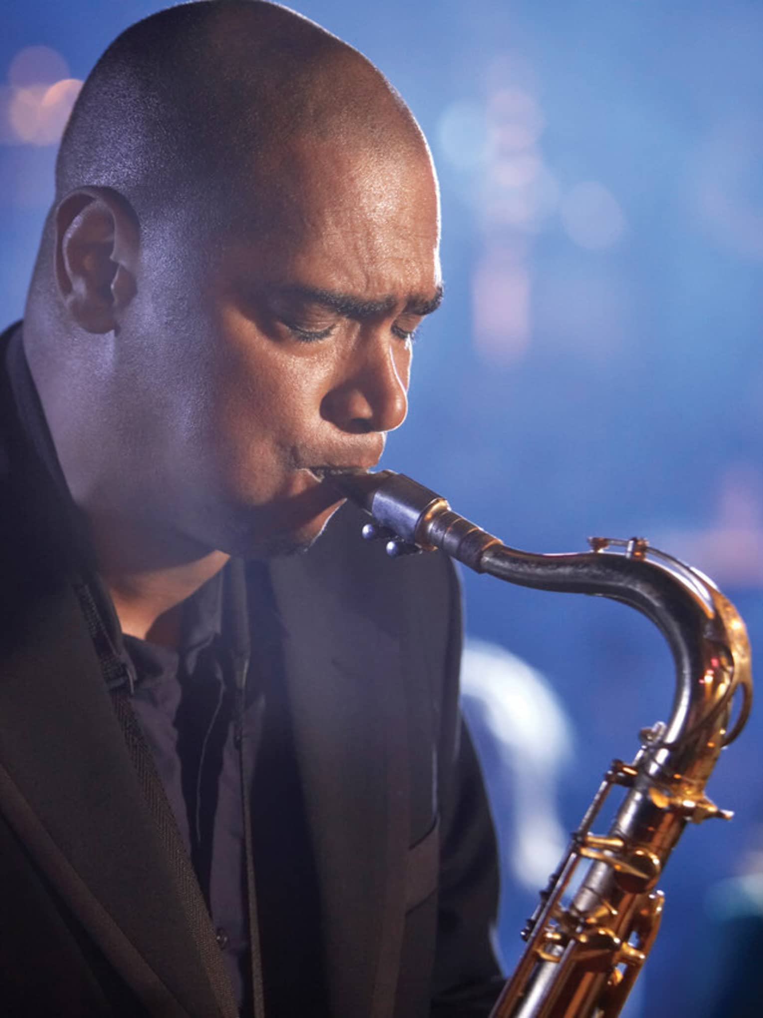 A close up of a man with his eyes closed, playing a saxaphone at a Jazz club in Ten Trinity