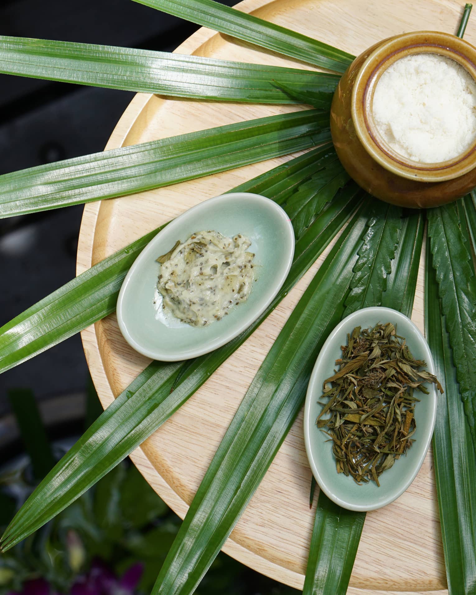 Pandan leaves laid out like a fan on a wooden table with a jar and small bowls of herbs and scrubs placed on top.