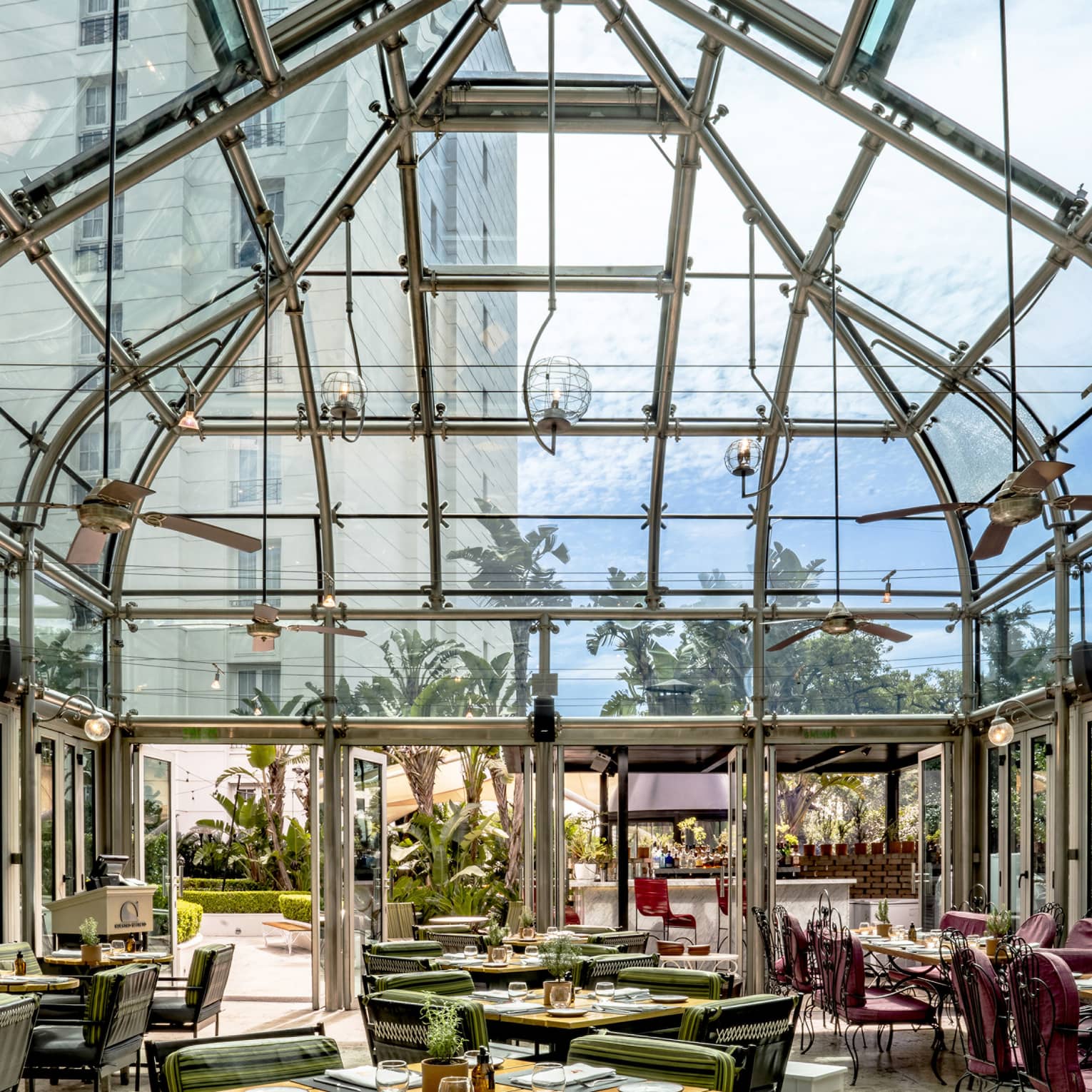 Restaurant dining room with tables set beneath a tall, retractable glass-and-metal ceiling