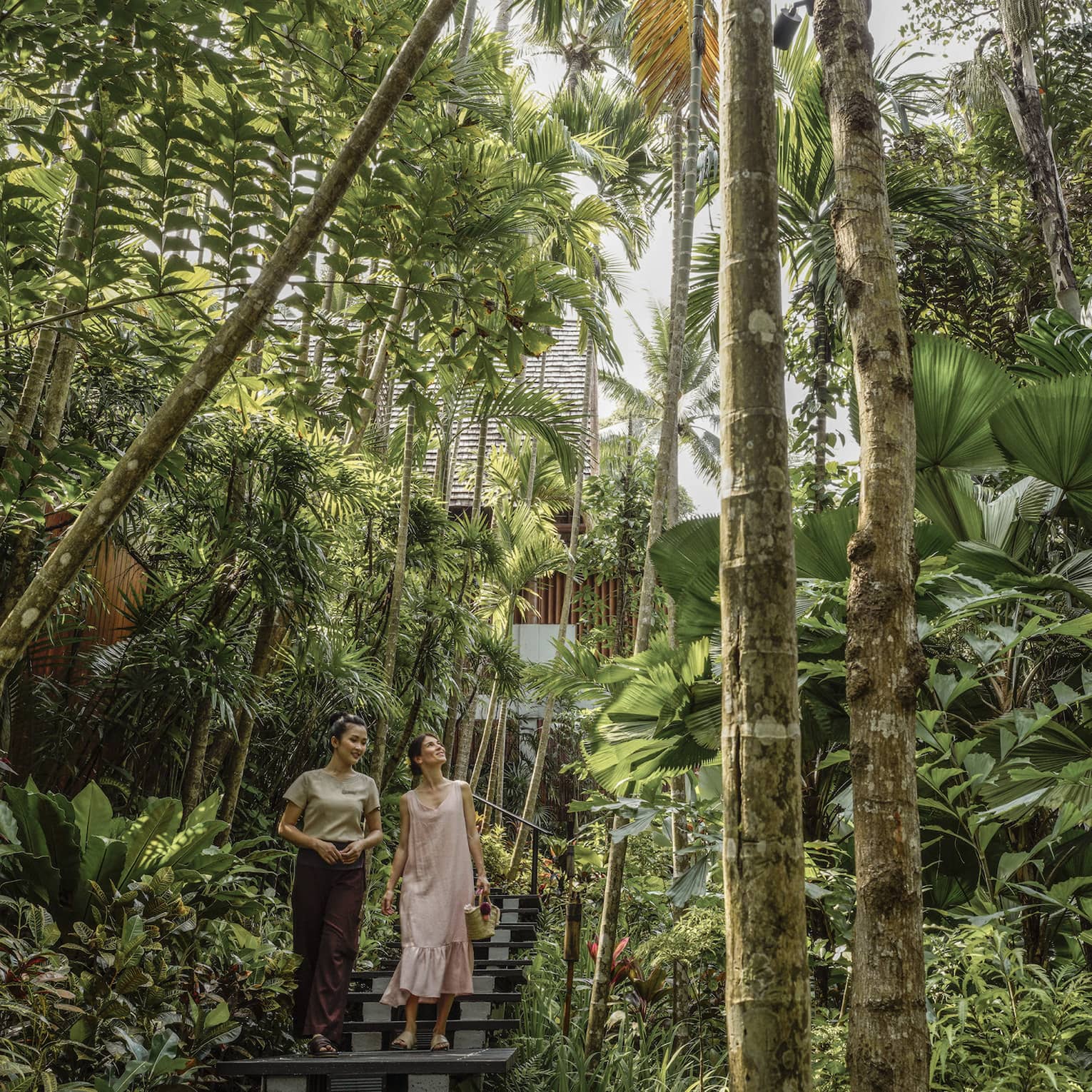 Female guest and spa staff member walk along foliage-lined pathway to the spa