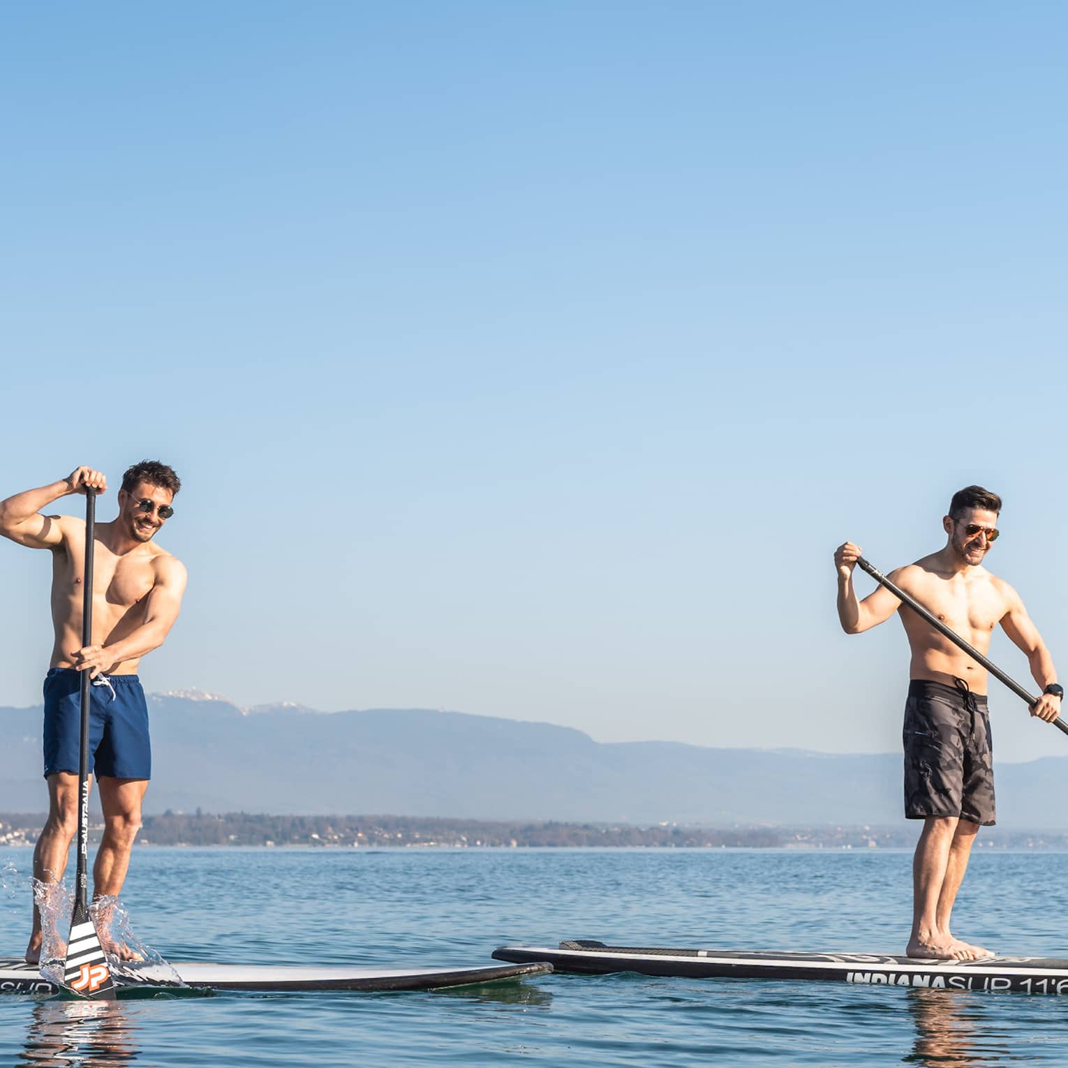 Two men stand-up paddleboarding on Lake Geneva