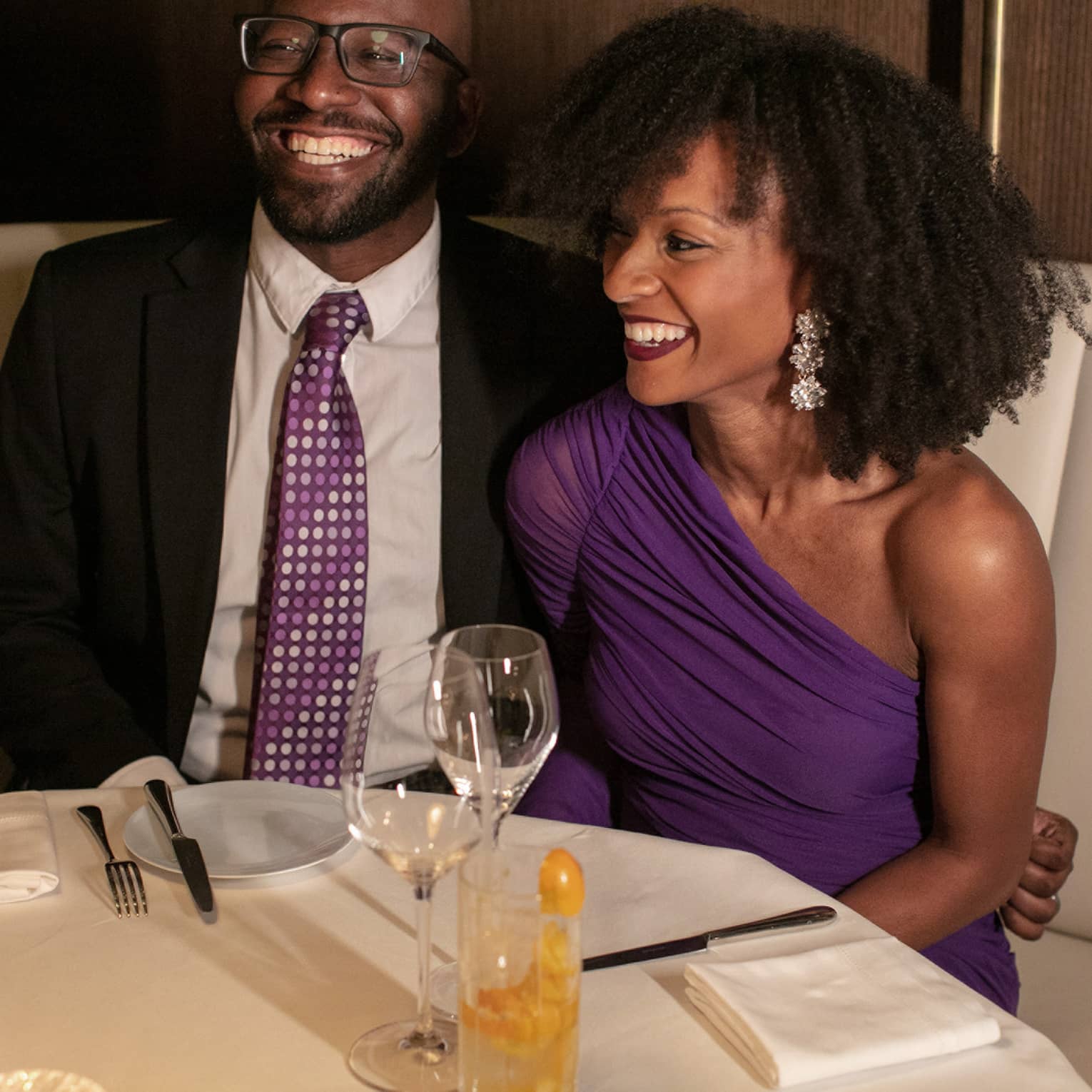 A man and woman in nice clothing sitting at a dining booth.