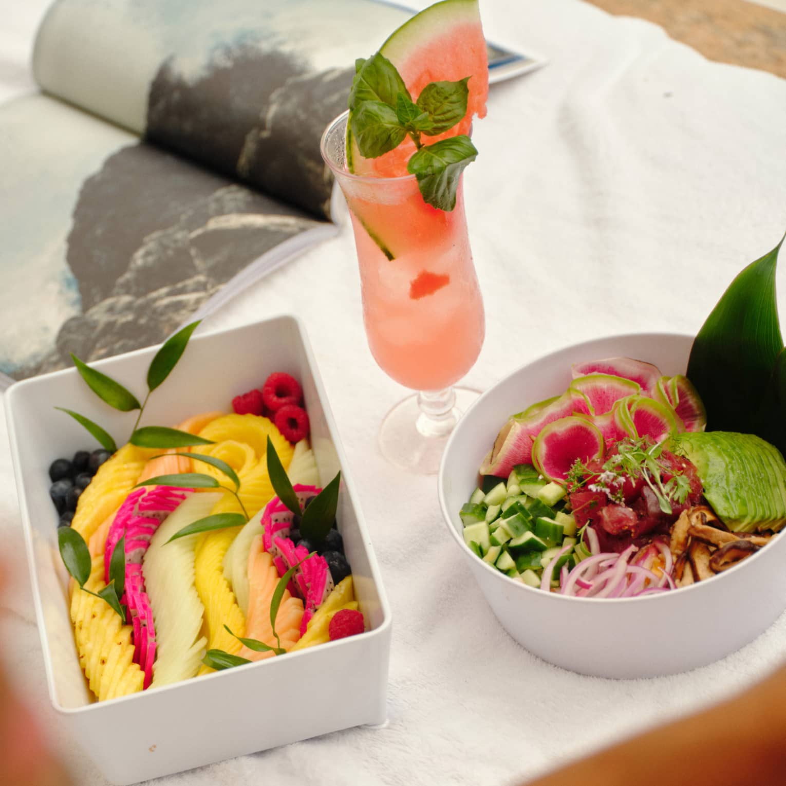 Fresh fruit and salad in white containers set on a day bed