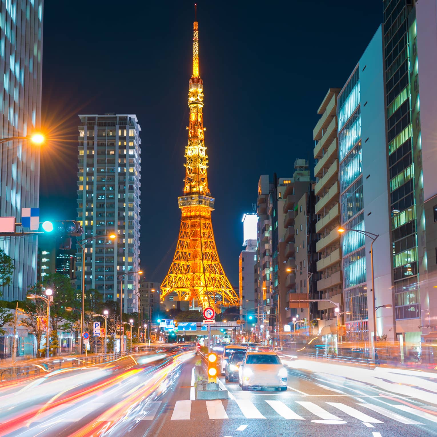 Long view down a brightly-lit street, the Tokyo Tower at the bottom, glowing in orangey hues against an inky-black sky.