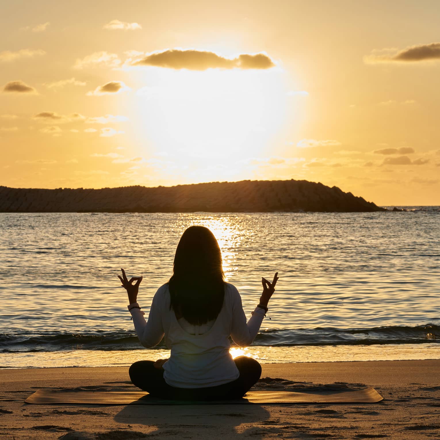 Woman meditates beachside at sunset