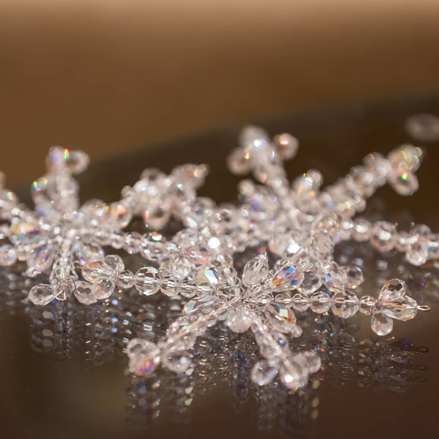 Three snowflake ornaments made of crystal beads placed on a dark table
