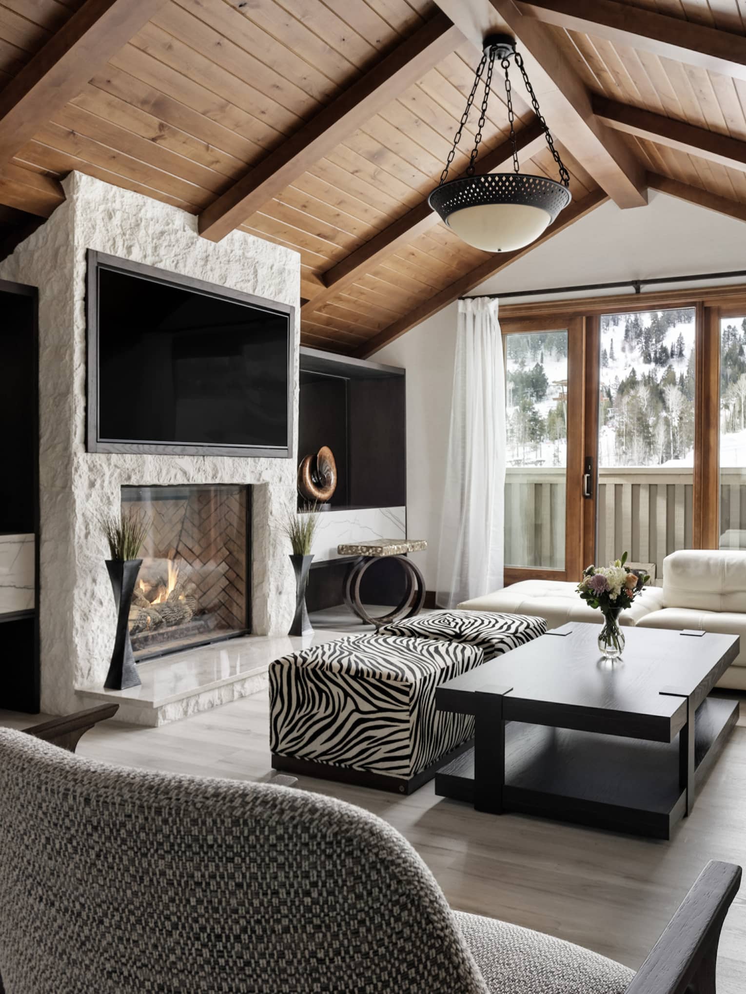 Mountain chic living room with large sofa, two grey arm chairs, vaulted wooden ceiling, stone hearth and TV