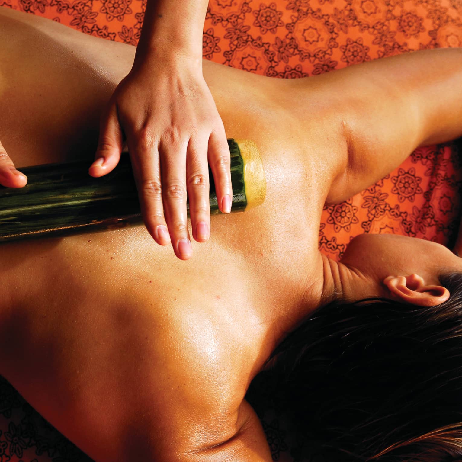 Spa staff rolls thick bamboo stick over woman's bare back, shoulders