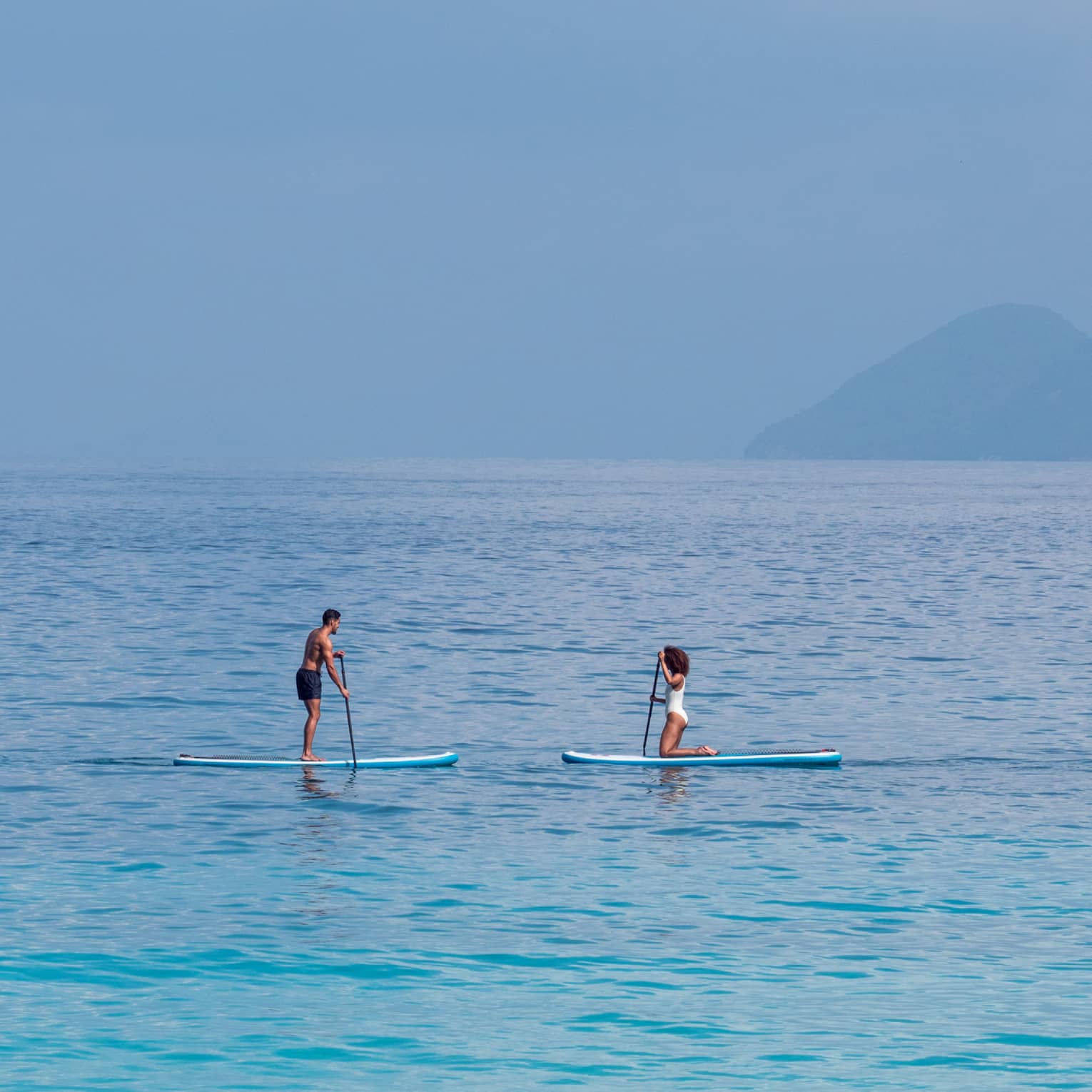 Man and woman paddle board on the open ocean, mountains visible through the fog