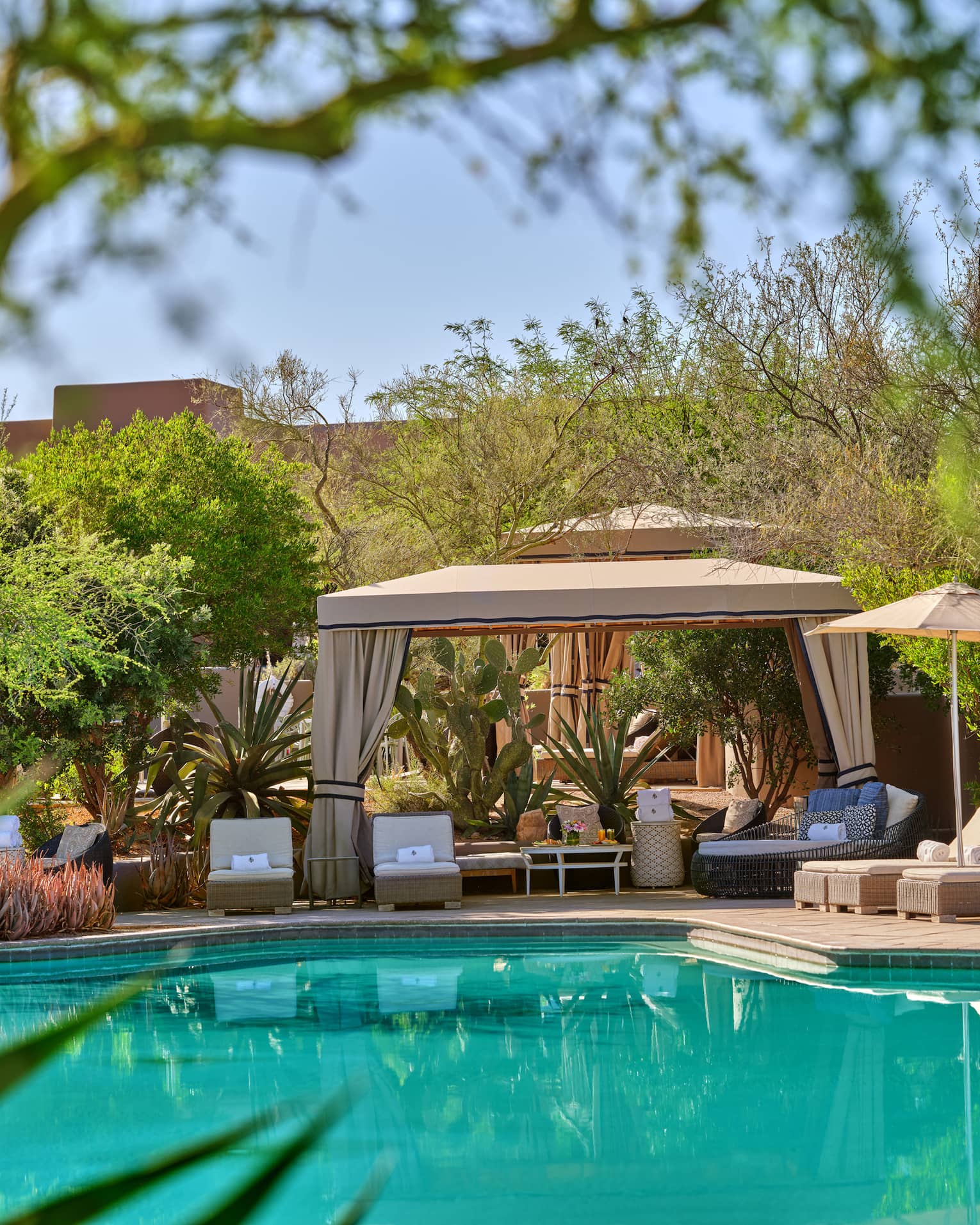 Blue pool with cabana and lounge chairs, surrounded by trees and greenery.