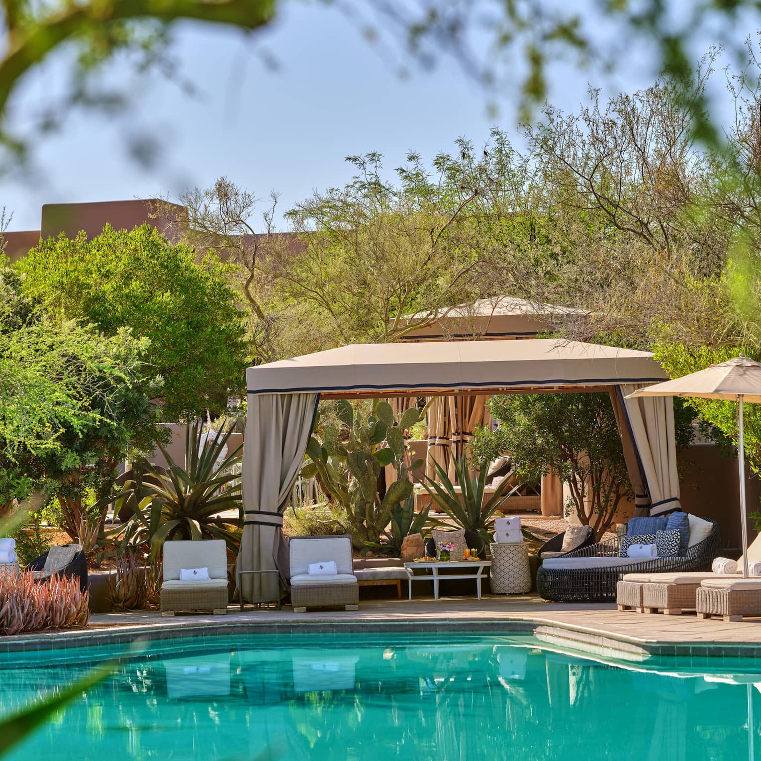 Blue pool with cabana and lounge chairs, surrounded by trees and greenery.