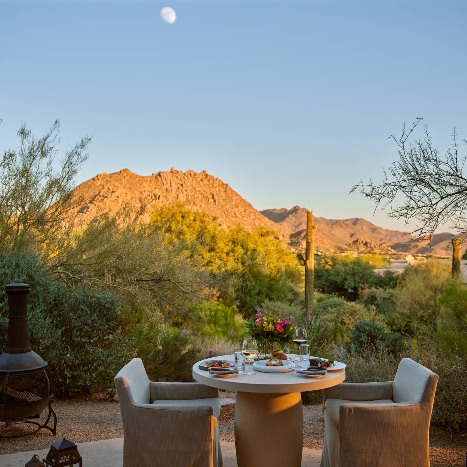 Two chairs and a table outside with lanterns and a view of the mountains.