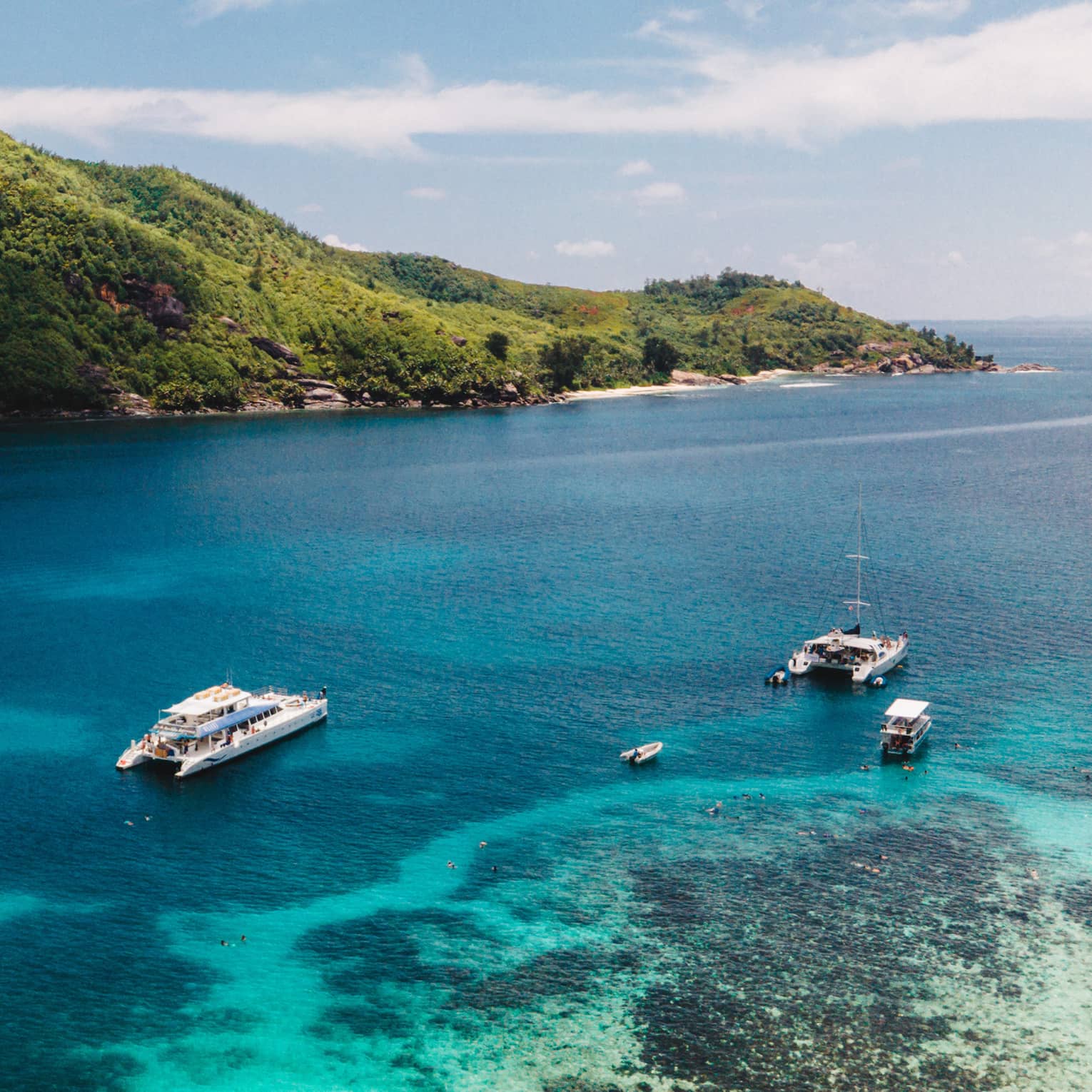 Two luxury yachts and two boats drift across turquoise water in Seychelles lagoon under tropical mountains