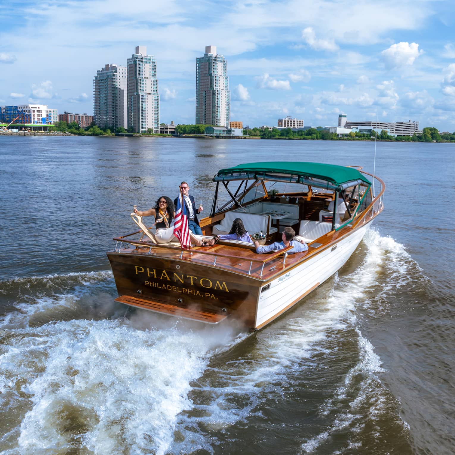 Guests on a boat in the water with city buildings in the background.
