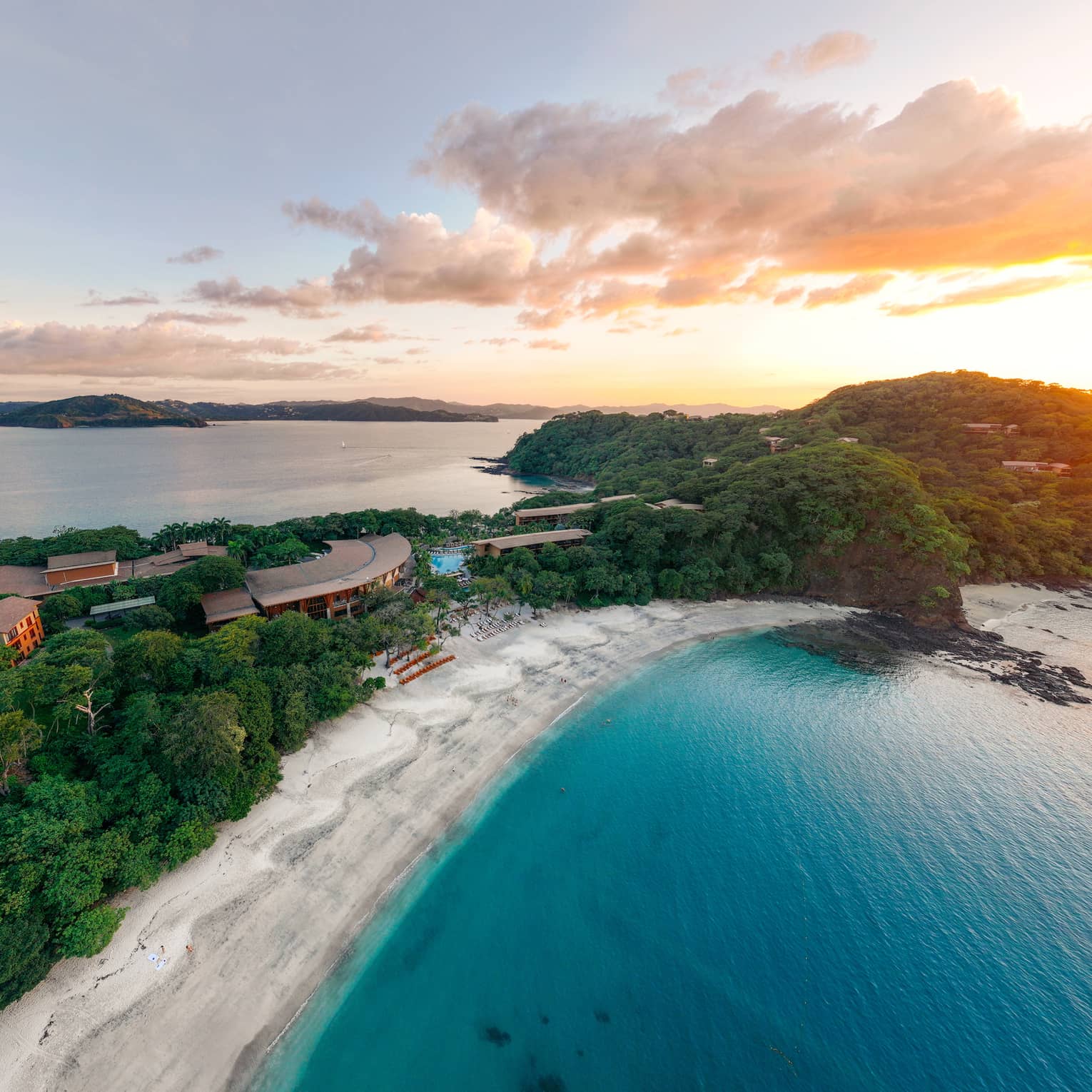 Aerial view of a narrow strip of beach with resort buildings and thick greenery in the middle and the ocean on either side