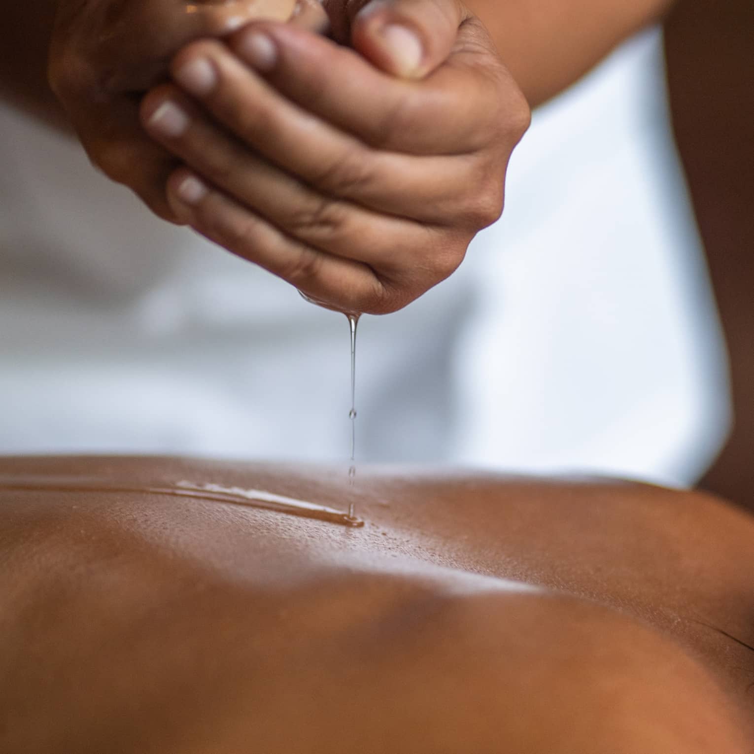 Delicate hands apply oil to a guest's back during a spa treatment