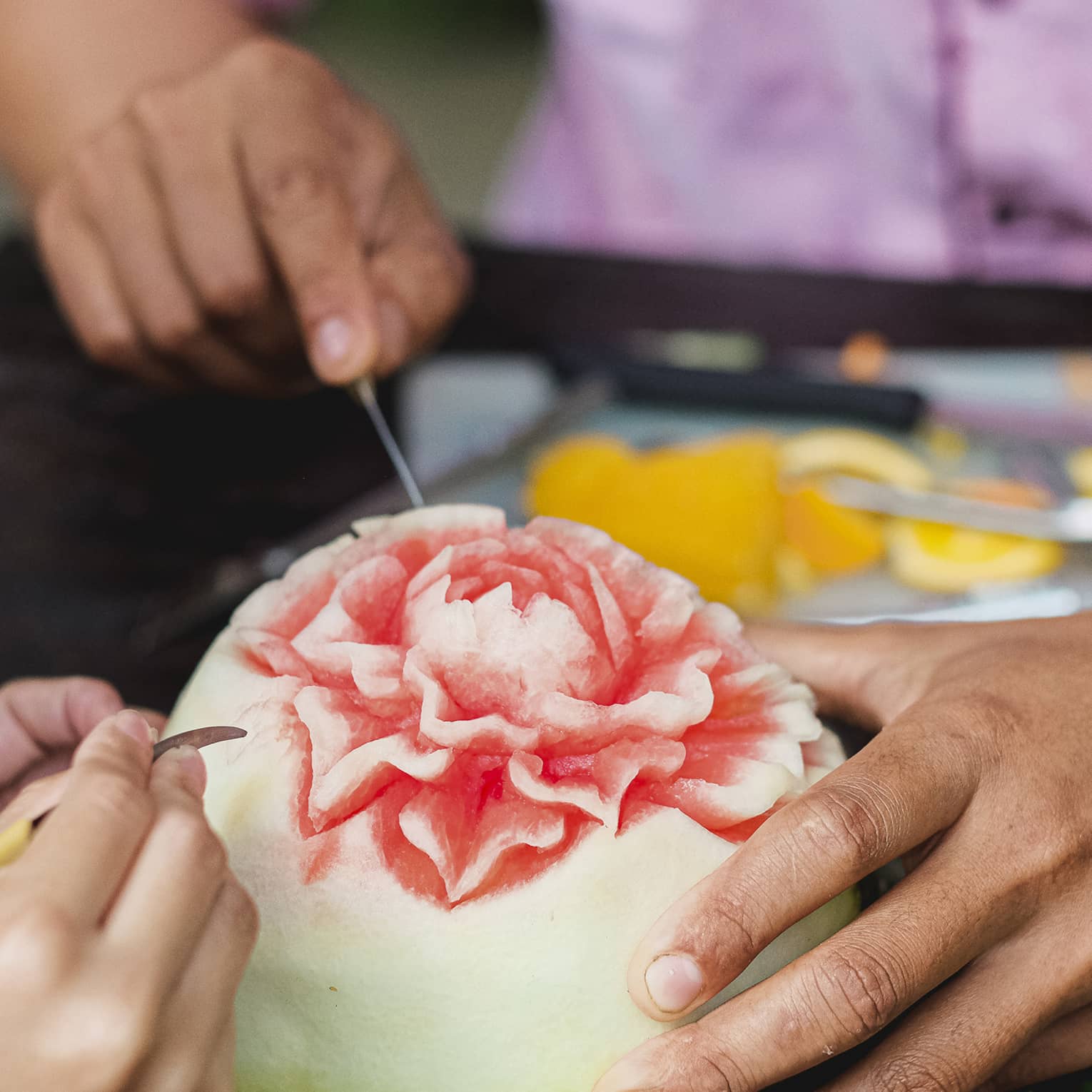 Close-up shot of man and child's hands carving intricate flower into watermelon
