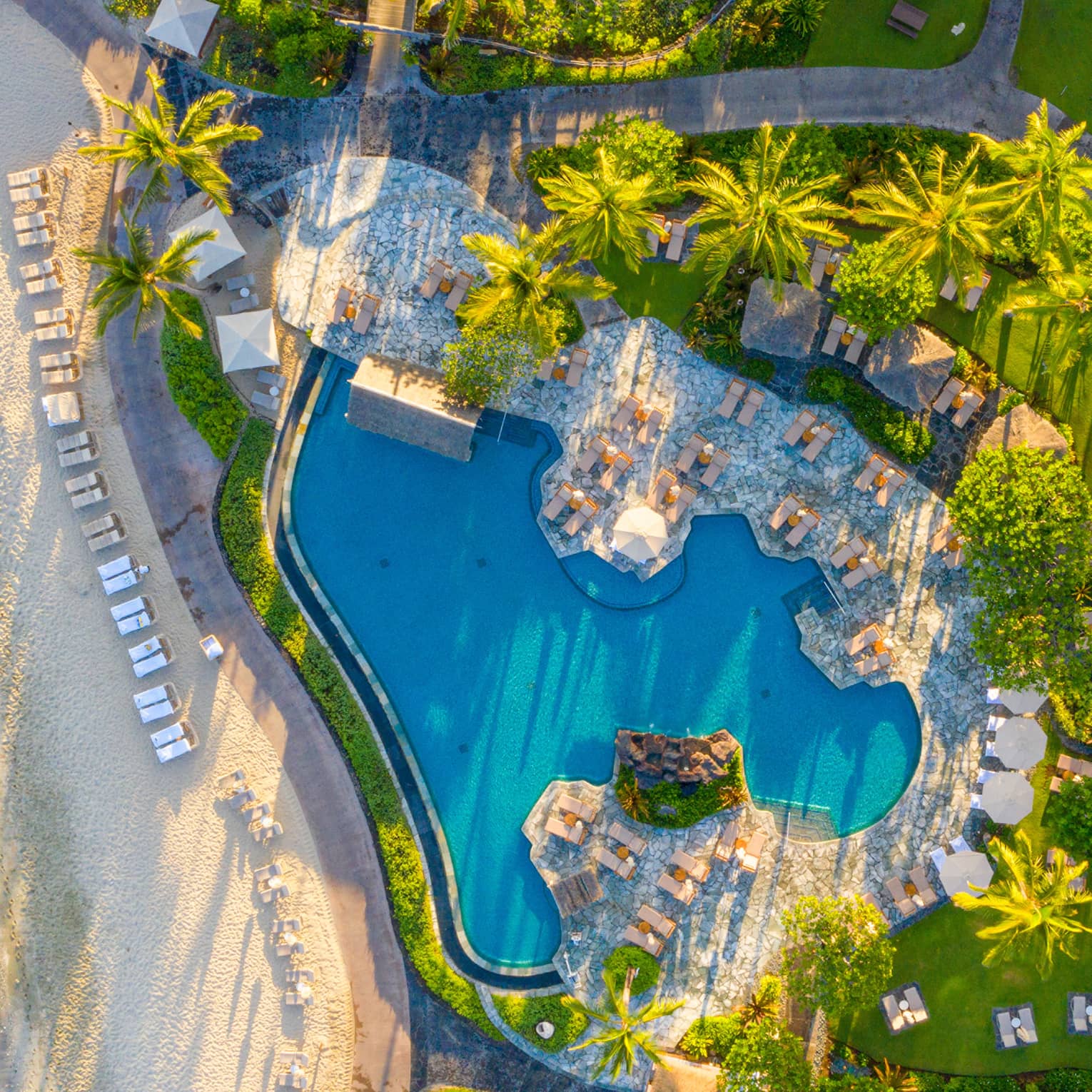 Aerial view of tropical resort pool next to a white-sand beach