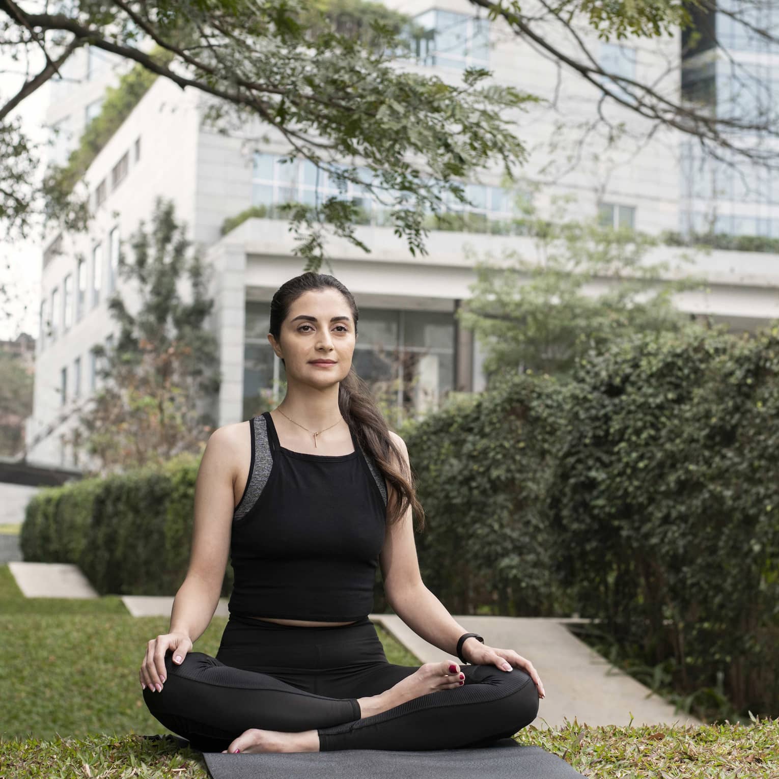 Person wearing athletic clothes and sitting on a yoga mat with their legs crossed.