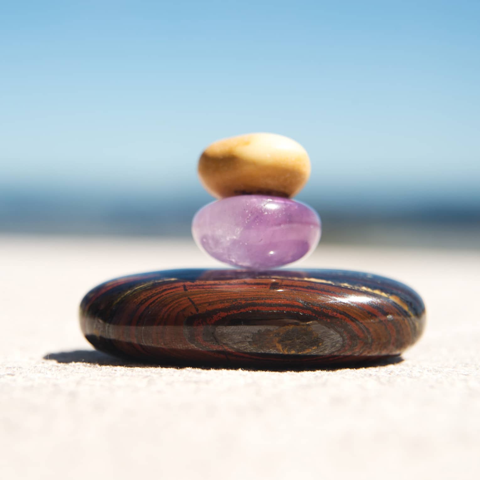 A small round amythest and a small round yellow crystal are stacked on top of a larger round, brown stone