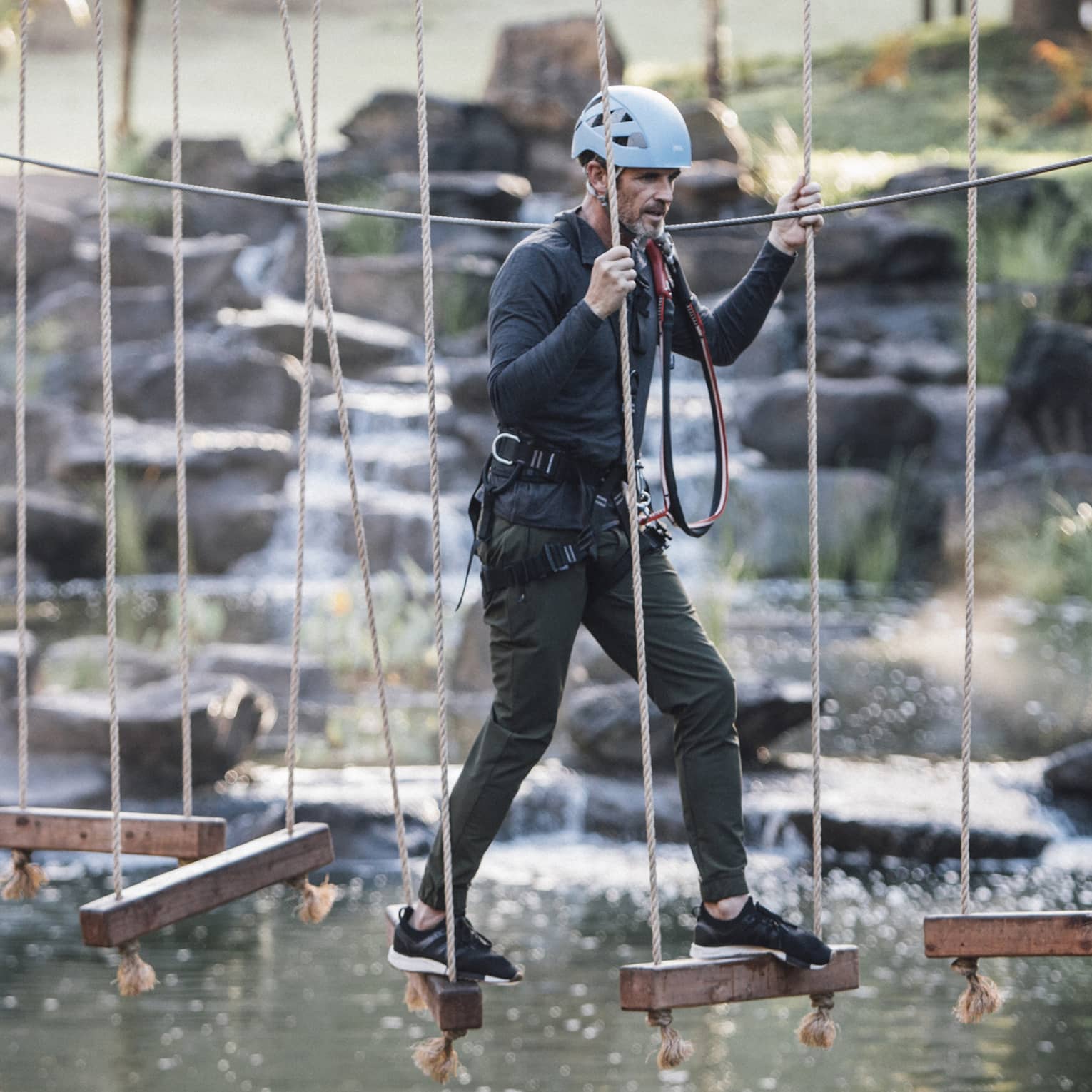 A man walks across hanging wooden blocks at ropes course