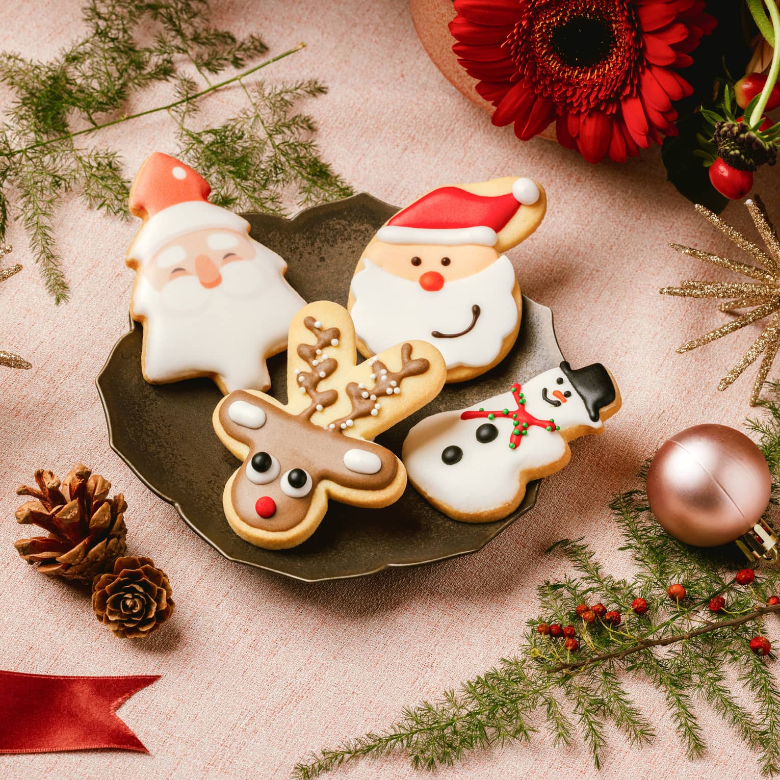 Assorted holiday cookies on small plate surrounded by Christmas ribbons, ornaments and pine tree fronds