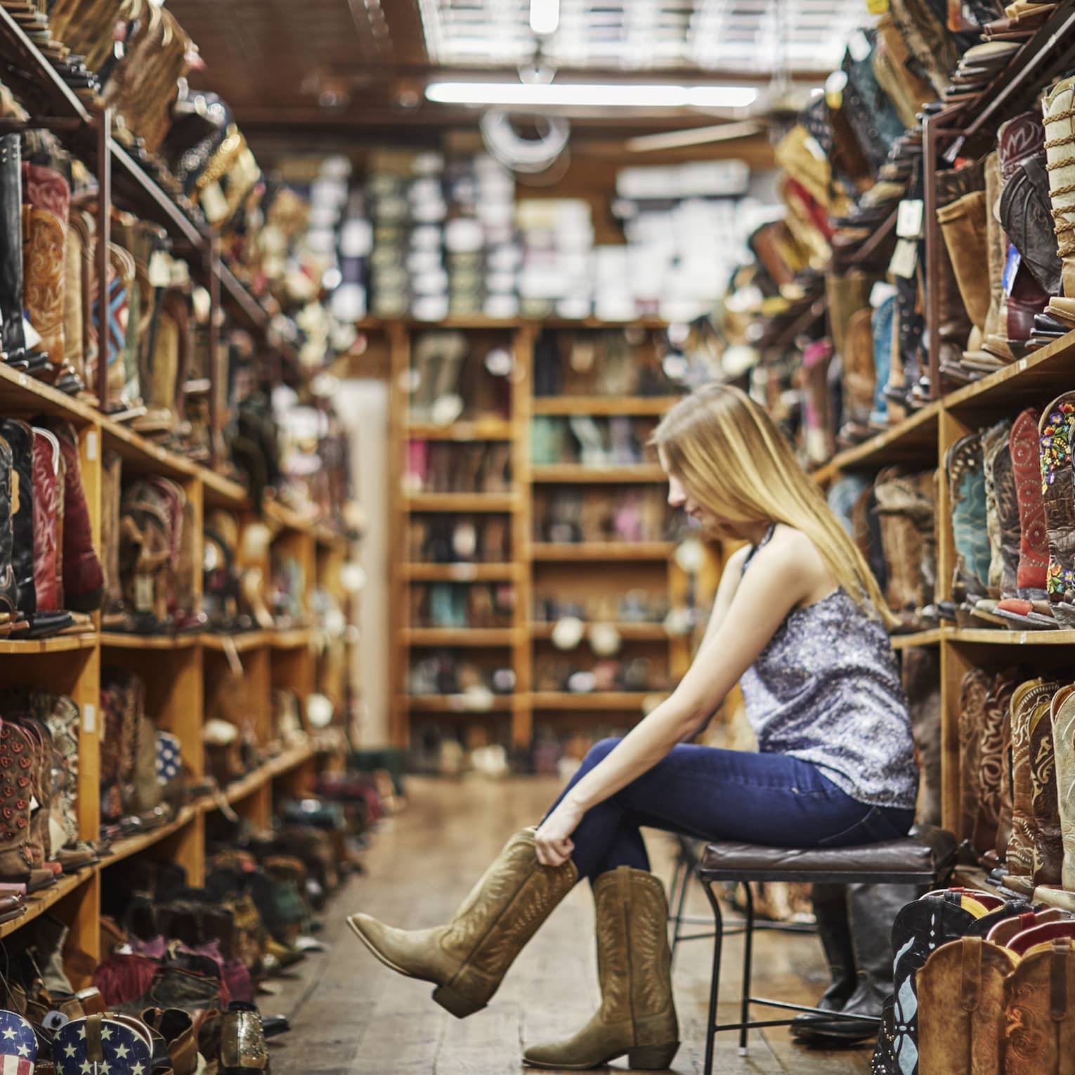 A woman trying on cowboy boots in a store full of them.