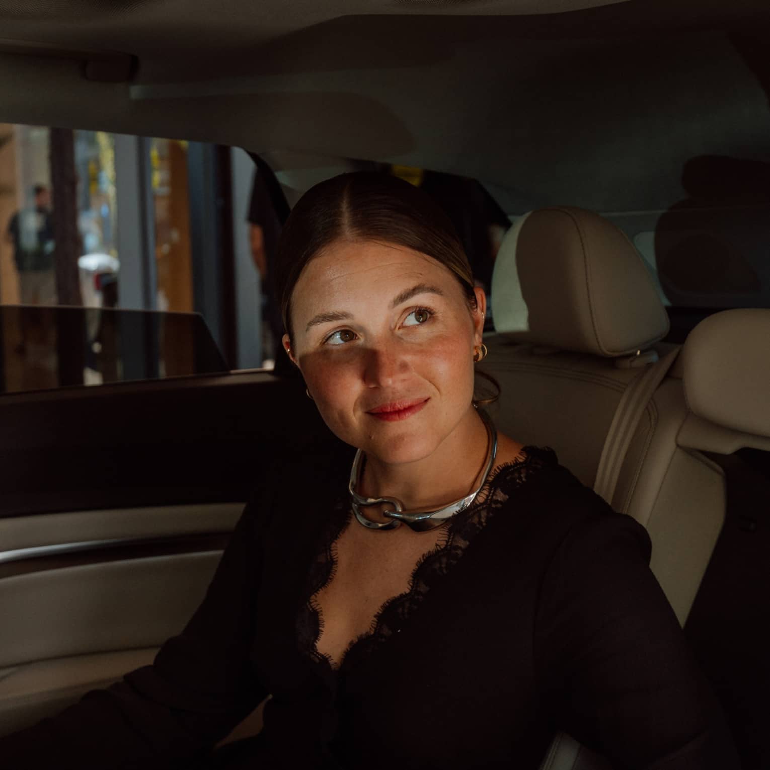 Person sitting in luxury vehicle backseat with windows slightly down