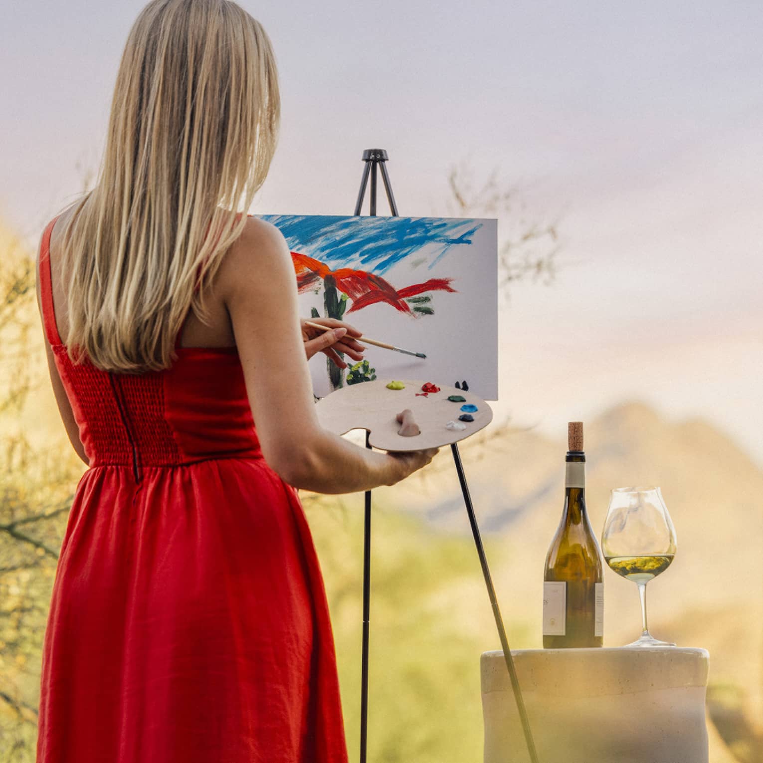 Person wearing a red dress and painting with a wine glass beside them.