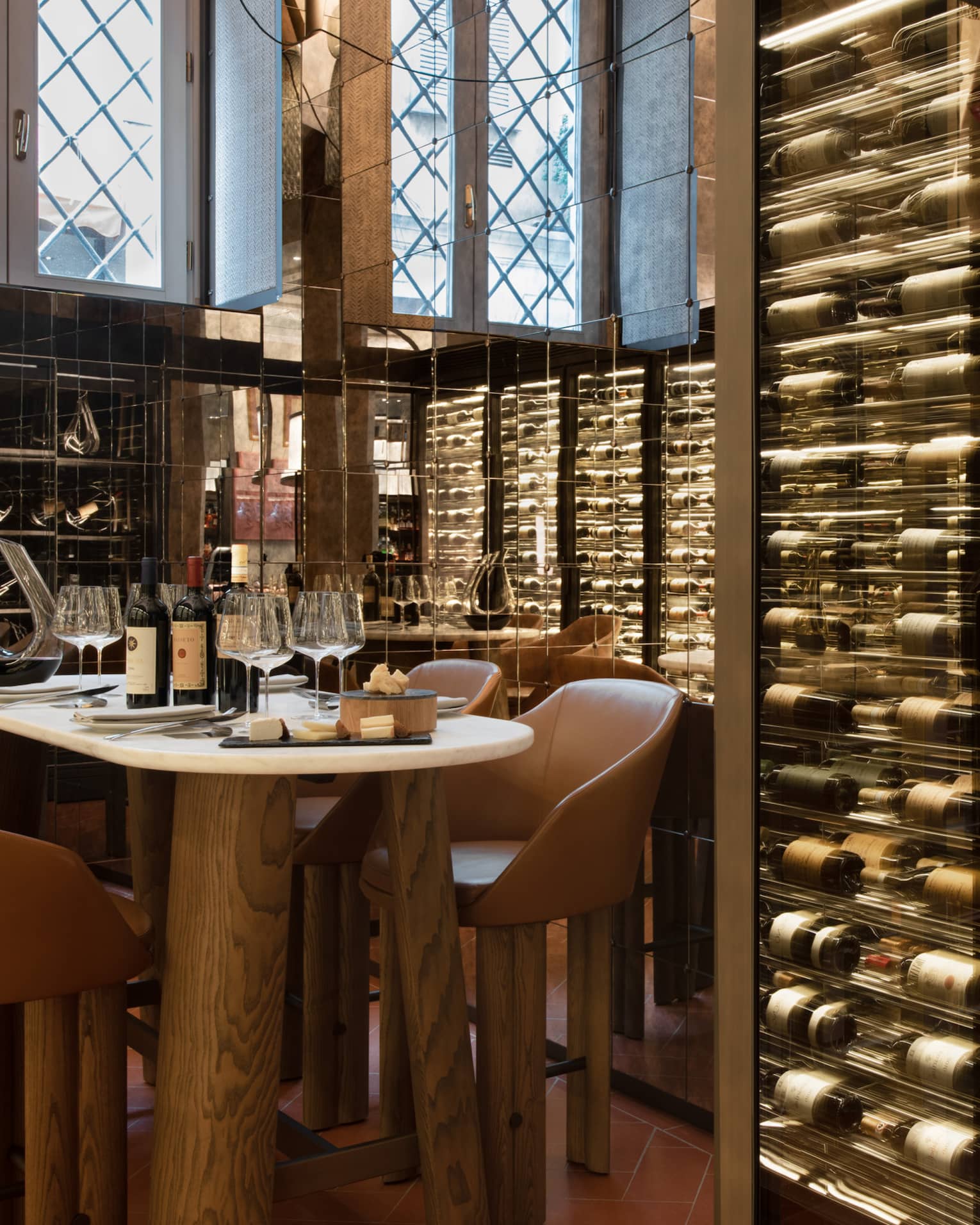 A table for four set within the mirrored walls of a wine cellar stocked with bottles displayed horizontally in glass cases.
