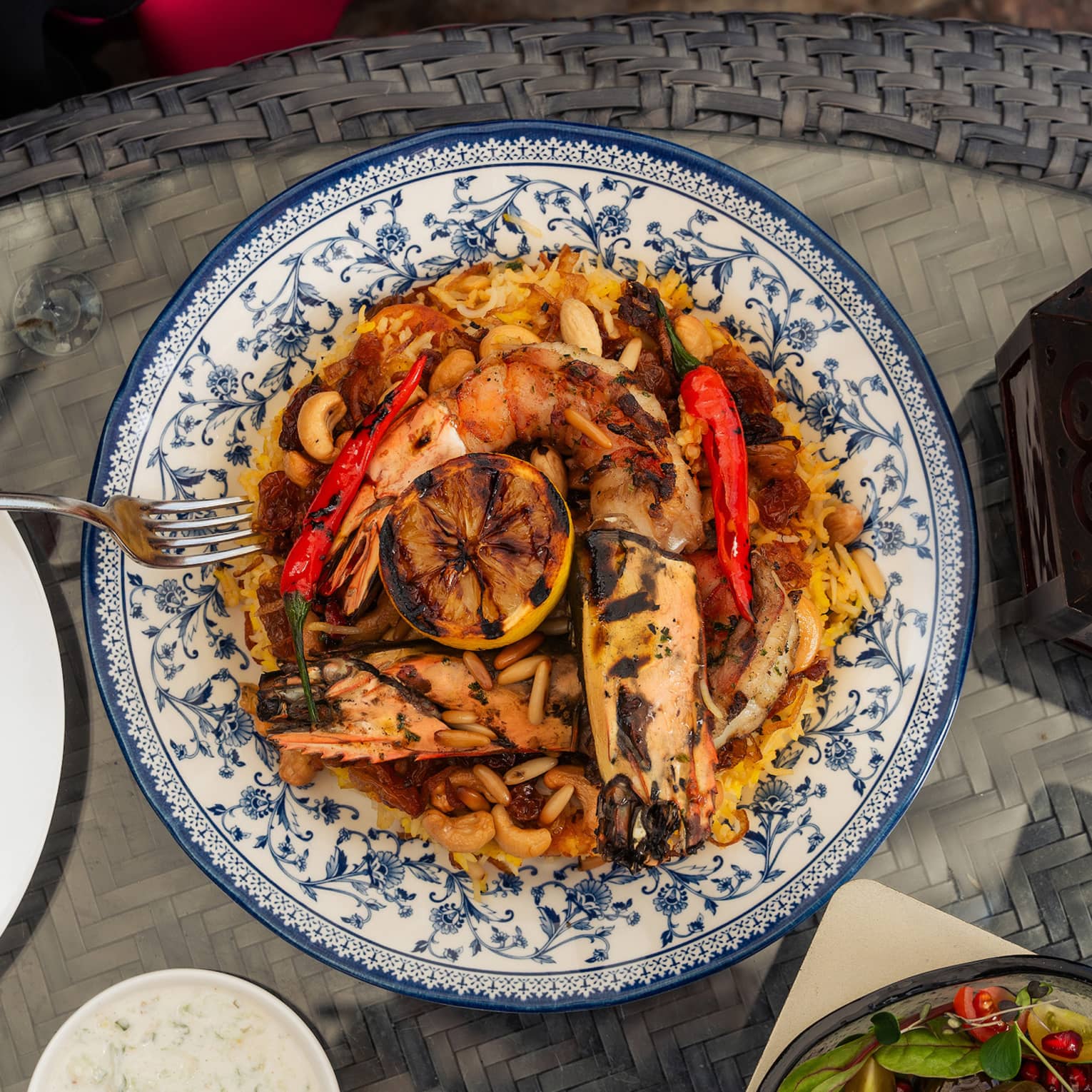 Deep gold risotto topped with grilled seafood, whole red chilis, raisins and nuts and a decorative grilled lemon slice.