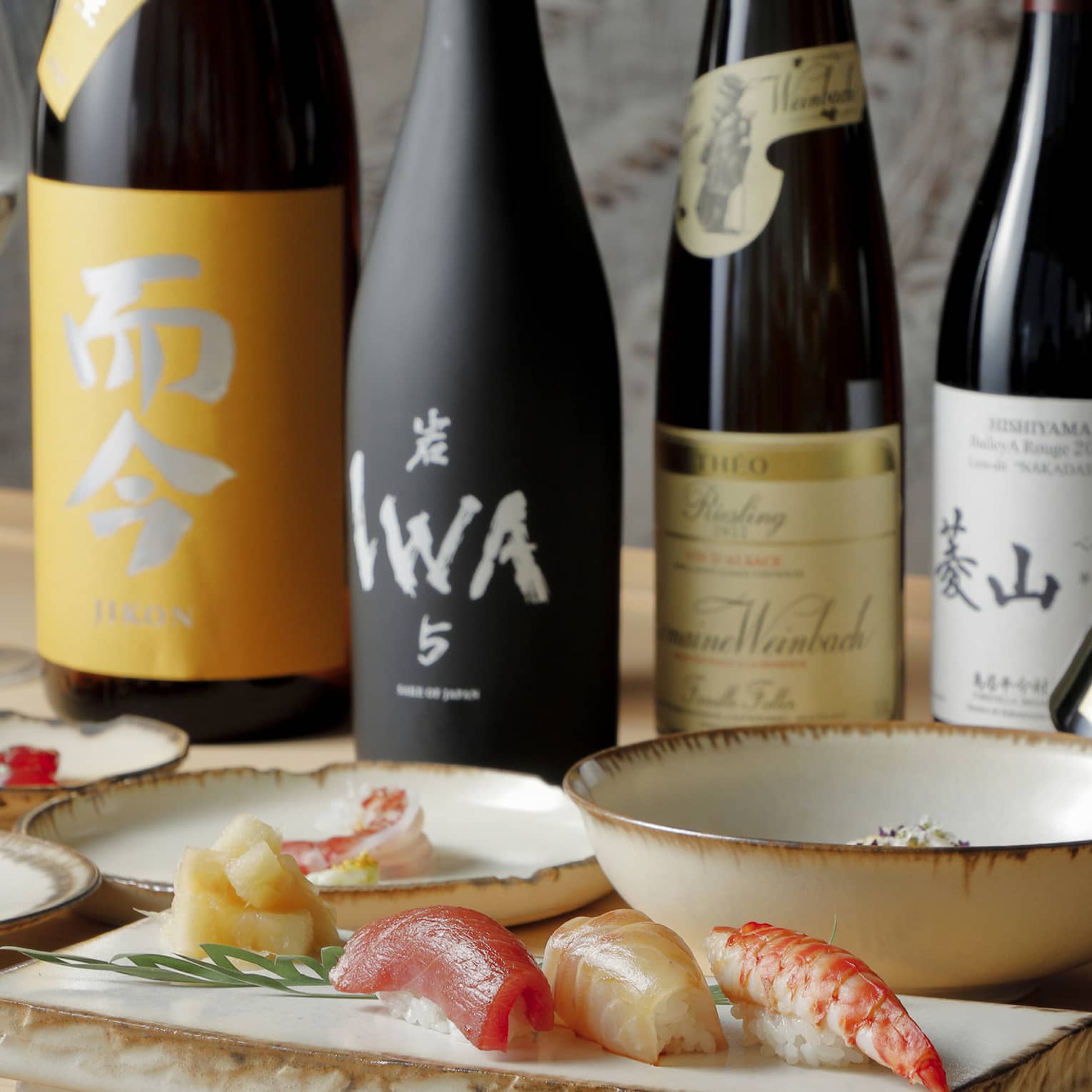 Bottles of sake and Krug champagne and glasses of wine behind dishes artfully laden with vibrant sushi and other delicacies.