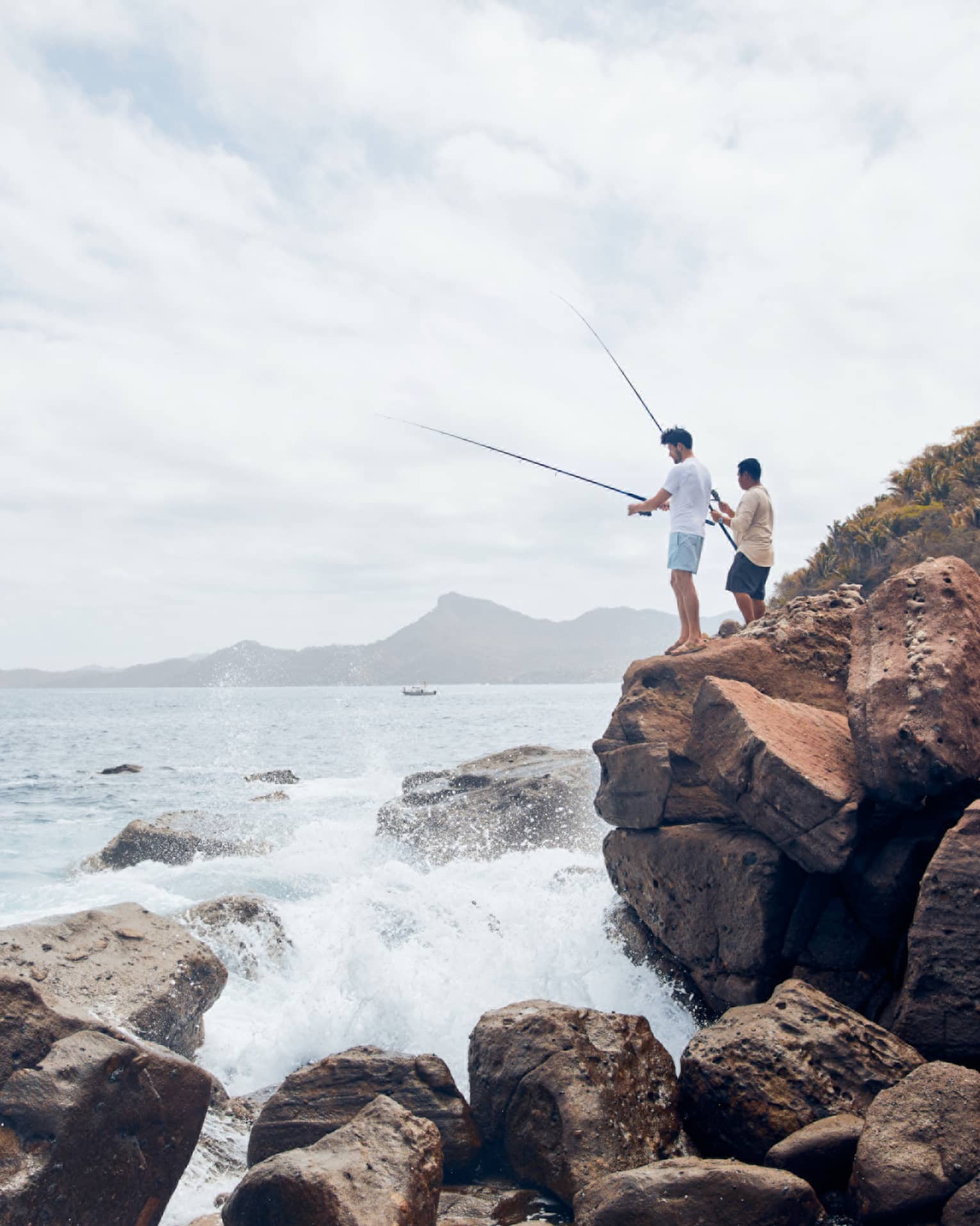 Two men on large rocks fishing in the ocean.