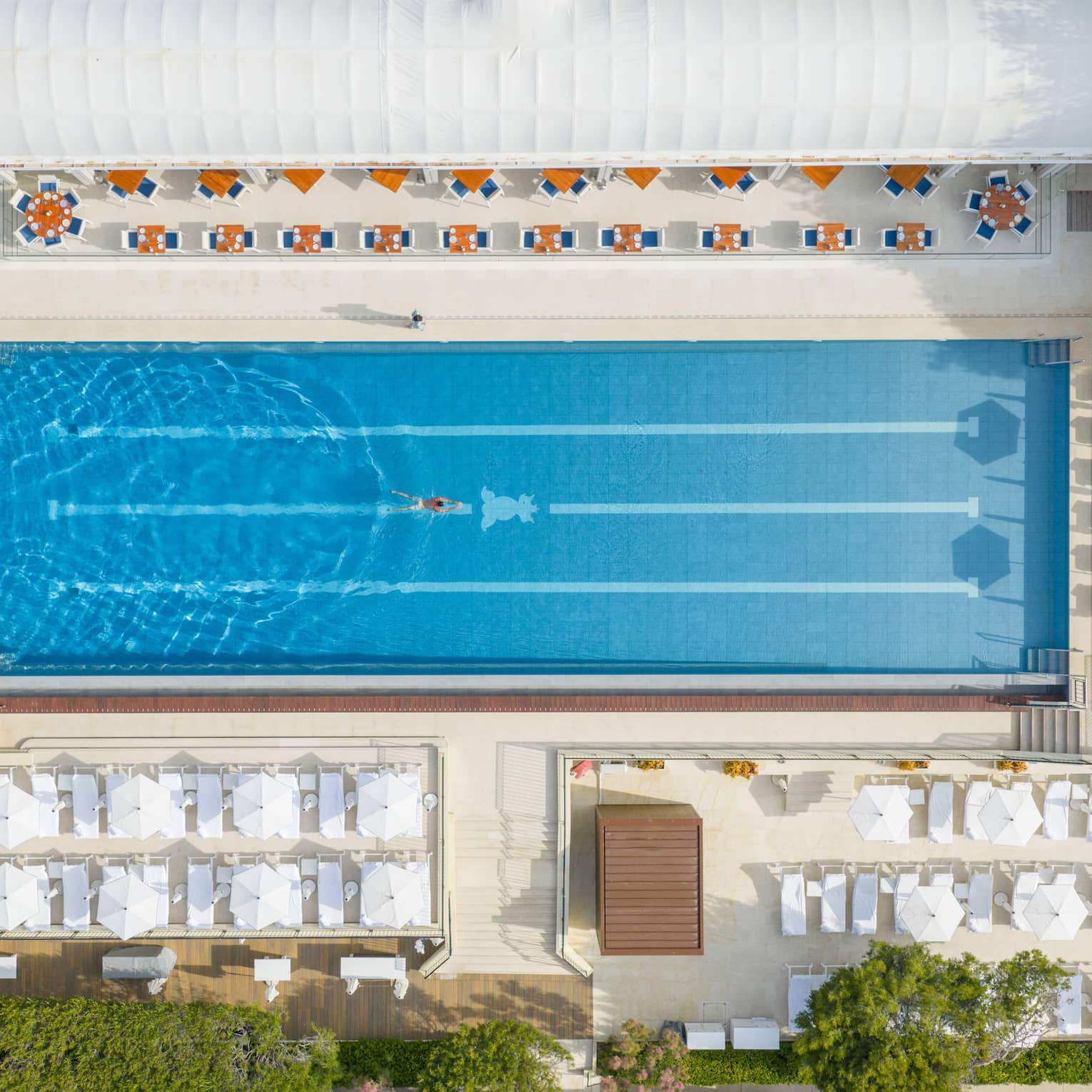 Aerial view of a luxury hotel, outdoor lap pool with surrounding white umbrellas and chairs