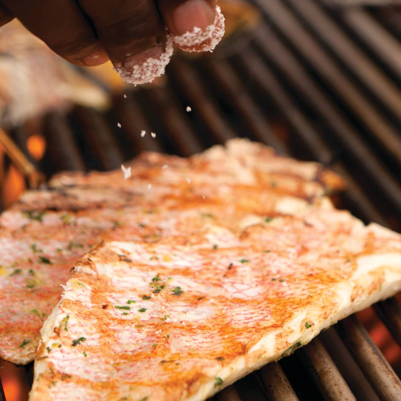 Close-up of hands sprinkling salt garnish on grilled fish on barbecue