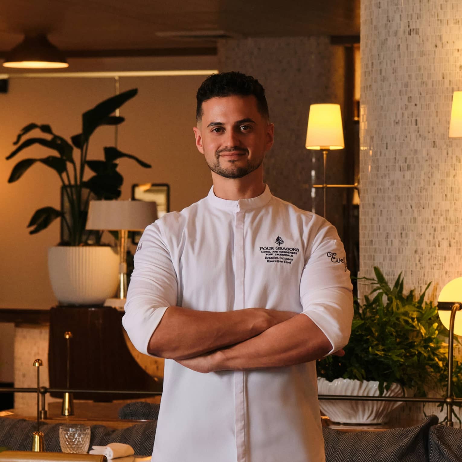 A chef stands in an elegant, softly lit indoor dining space.