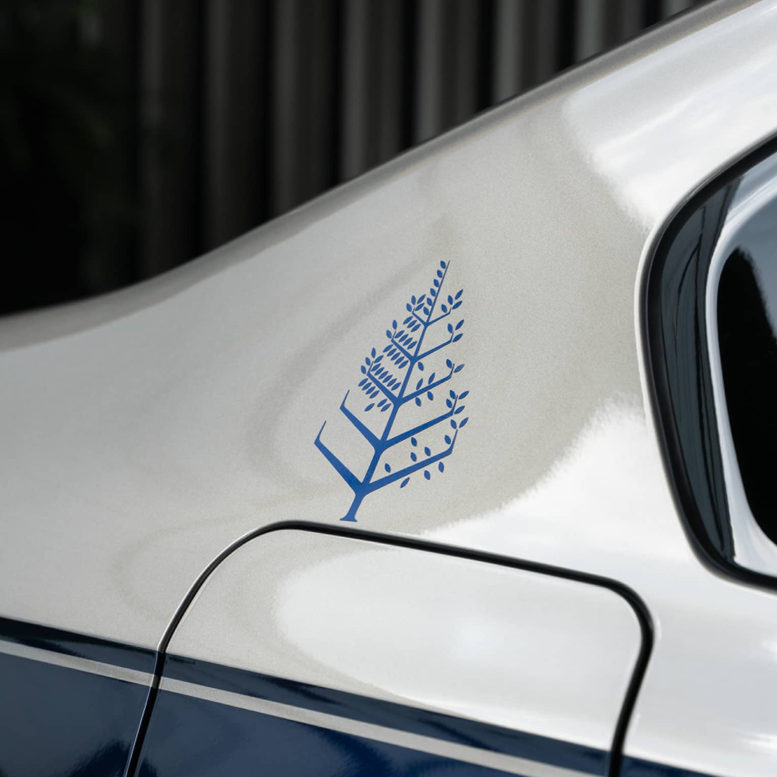 Close-up of the blue Four Seasons tree logo above the fuel tank door of a glossy silver and blue luxury car.
