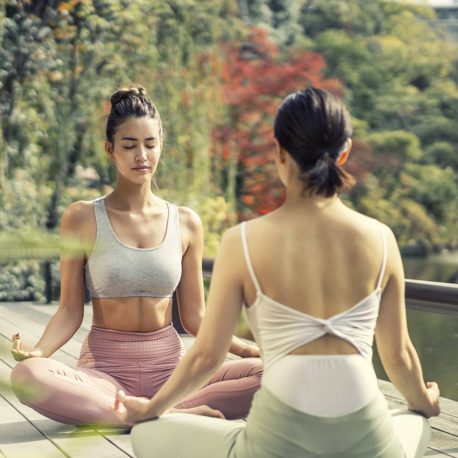 Two women sit cross-legged in a yoga pose in the Shakusui-en pond garden