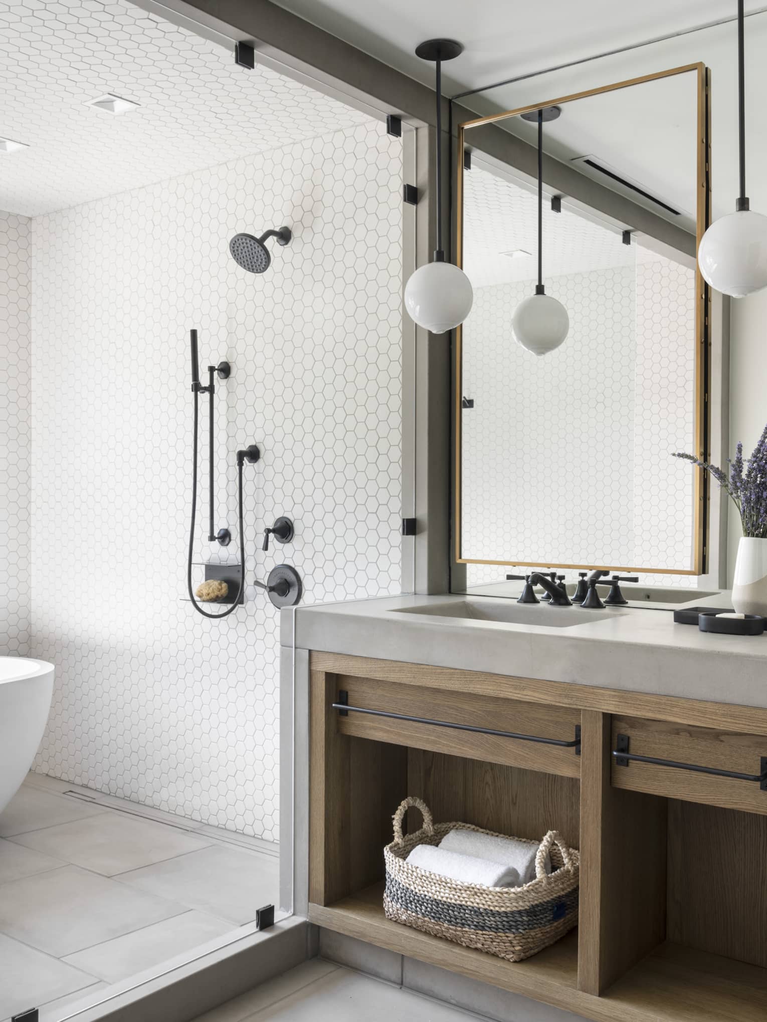 Luxury resort bathroom with a freestanding bathtub, walk-in shower, double vanity with wooden cabinetry, mirrors, hanging globe lights and lavender decor