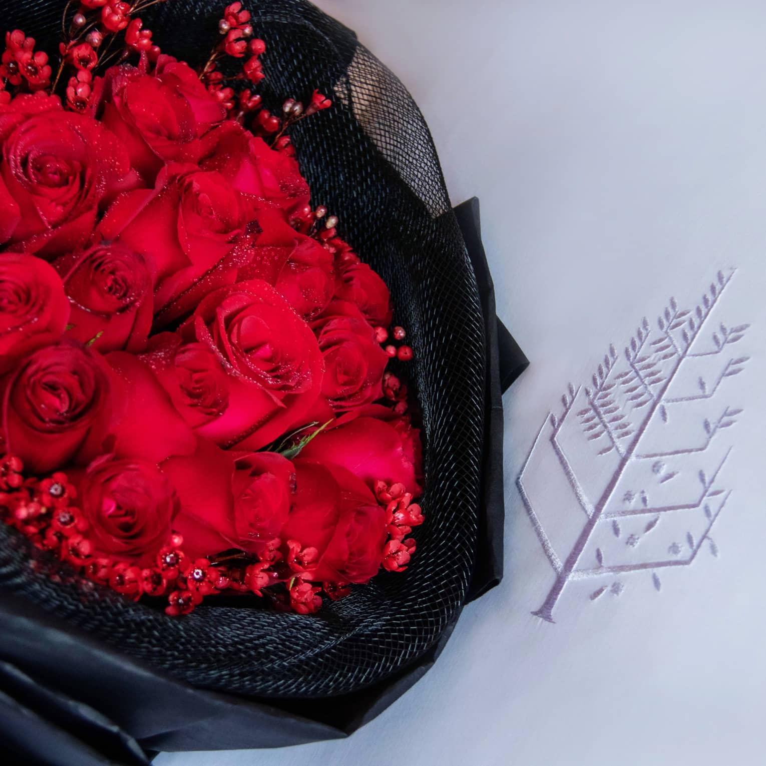 Bouquet of red roses wrapped in black fabric laying on a white pillow with the Four Seasons logo