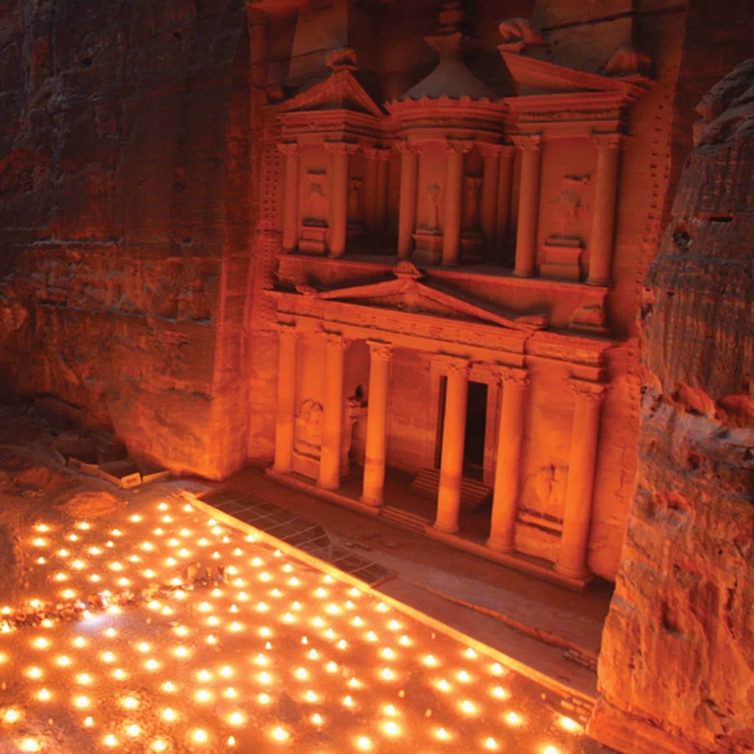 Aerial night view of Petra landmark, historic ruins built into cliffs, with lanterns scattered across the ground