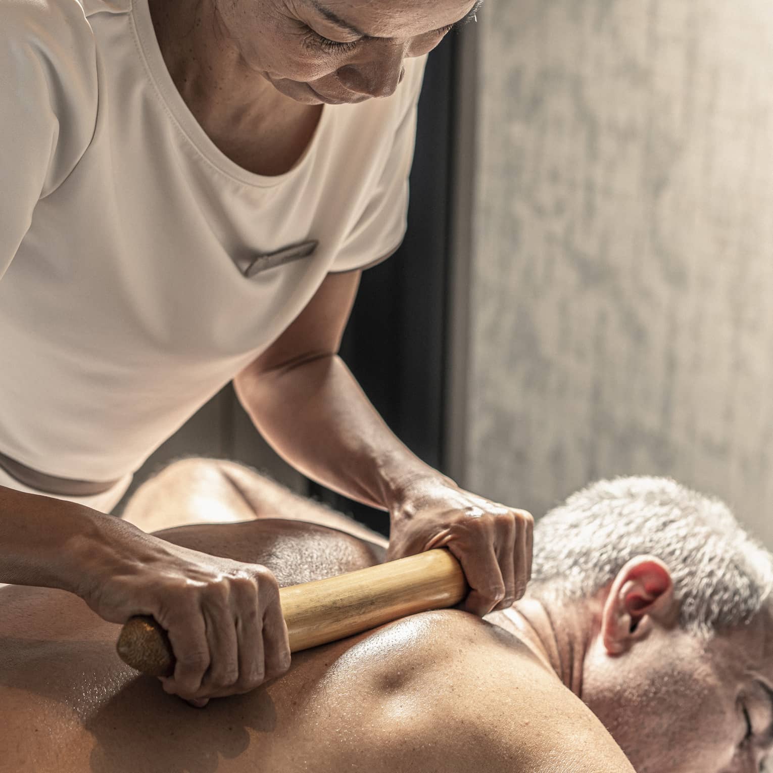 Massage therapist performs a bamboo massage on male guest