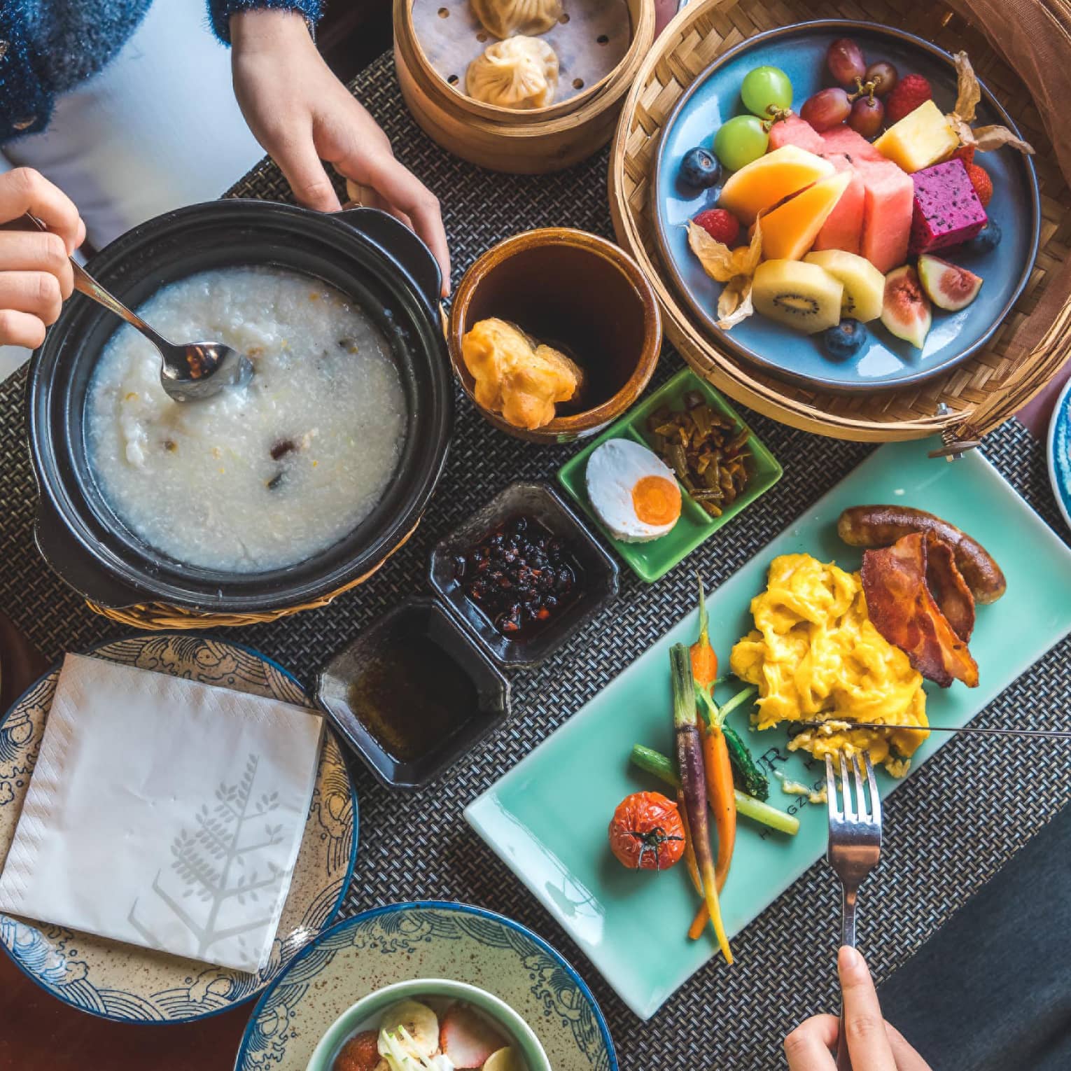 View from above as two guests savour a sumptuous array of vibrant dishes, including pastries, congee, fresh fruit and coffee.