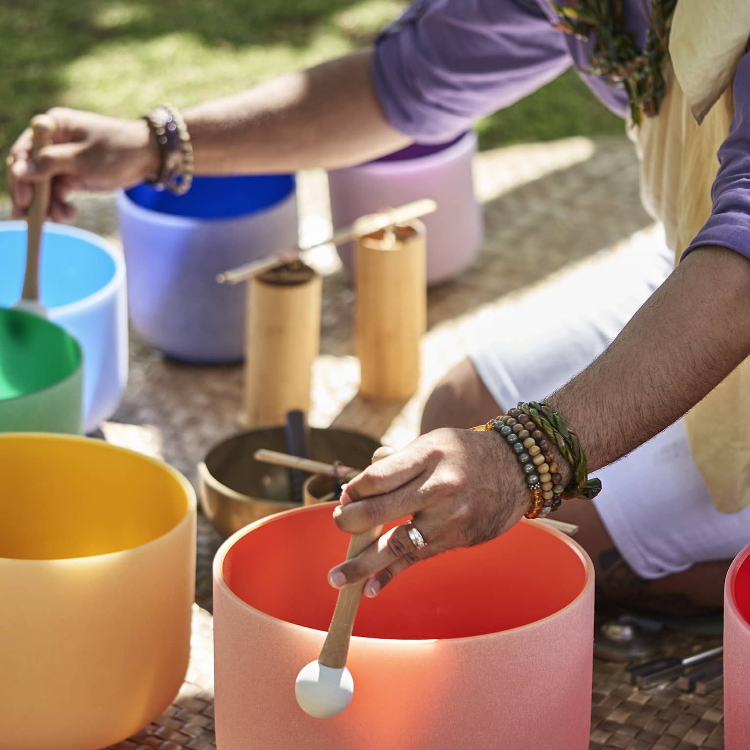 Close up of a man's hands using mallets to play a row of colourful crystal sound bowls