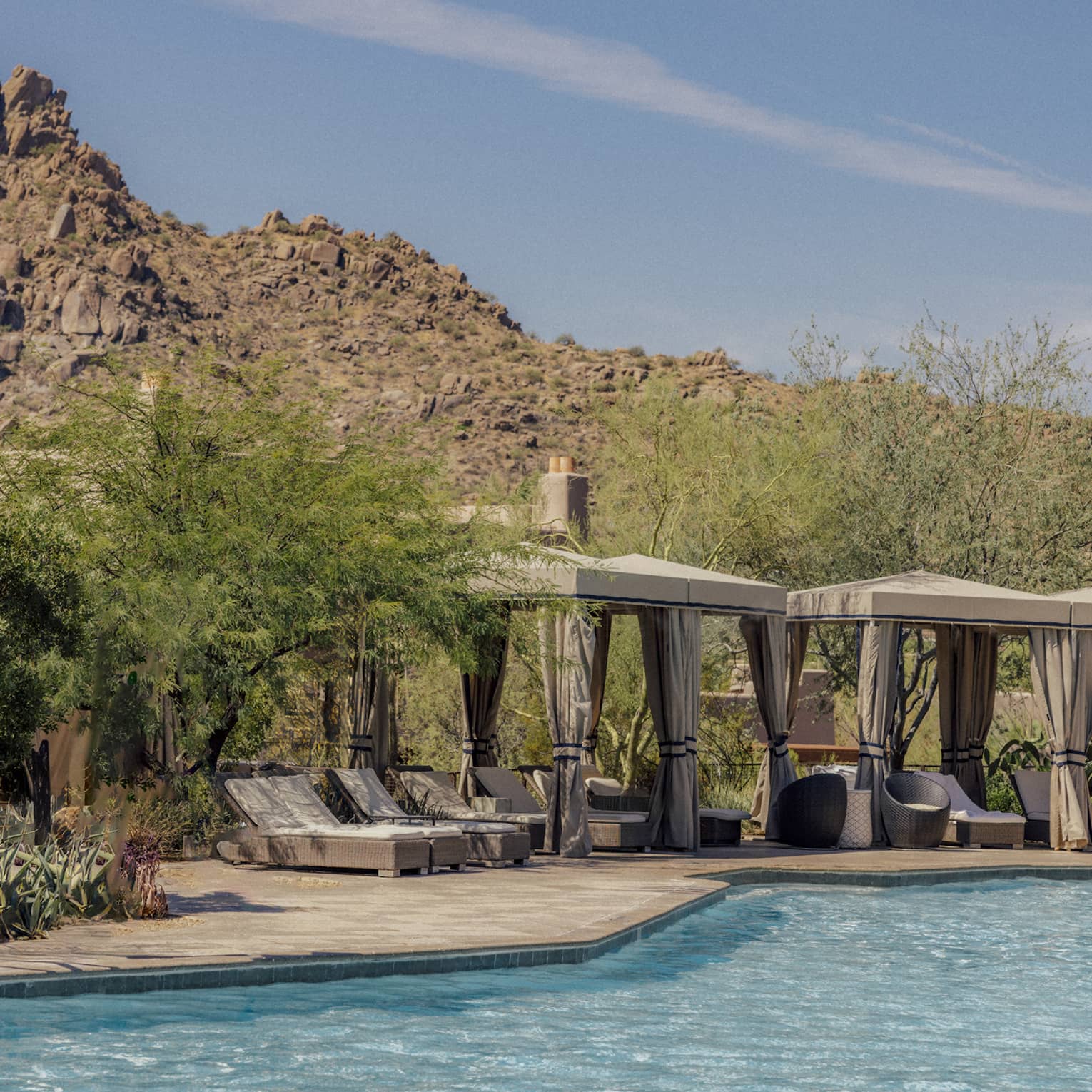 Pool with cabanas that have lounge chairs with a backdrop of the mountains.