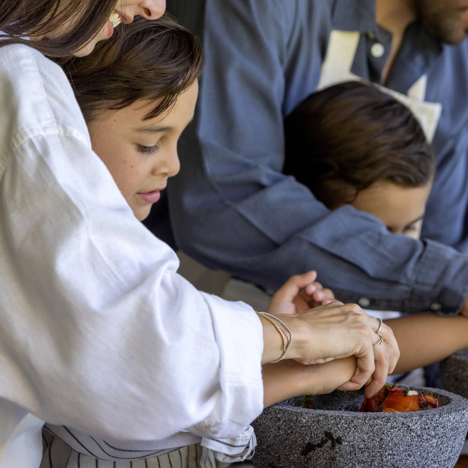 Two adult guests helping two young guests cook.