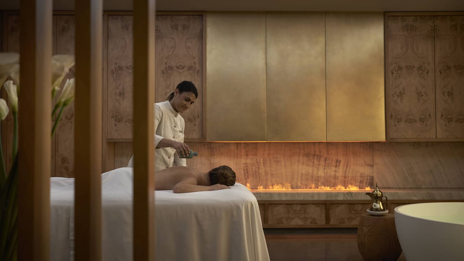 Spa therapist pours oil on back of person facedown on spa table
