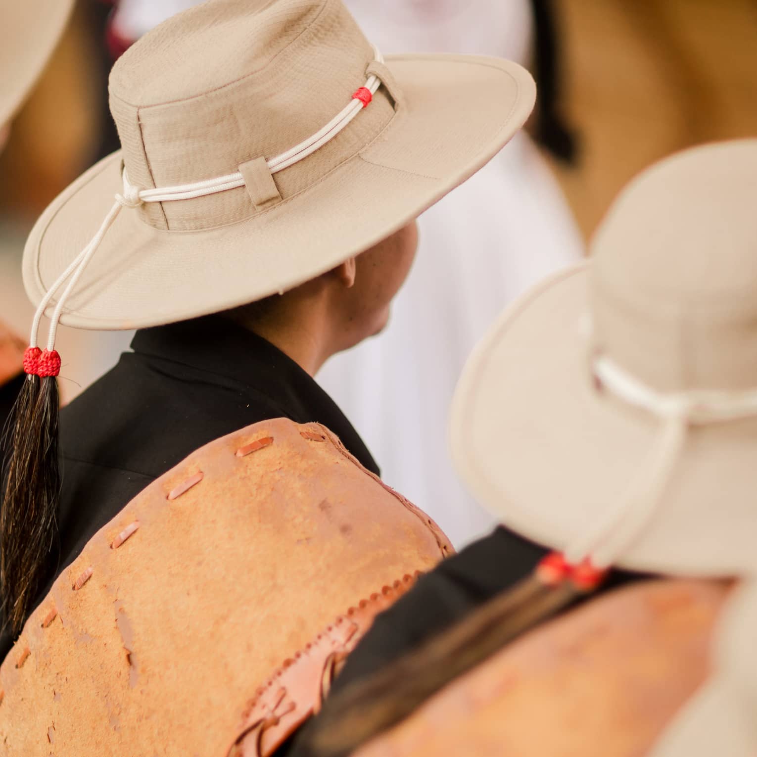 Three people in a crowd wearing beige hats with a tie around the top