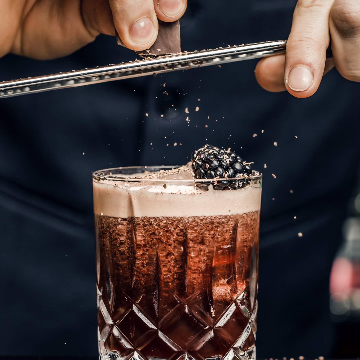 Churchill Club bartender shaves garnish over cocktail in crystal rock glass with blackberry